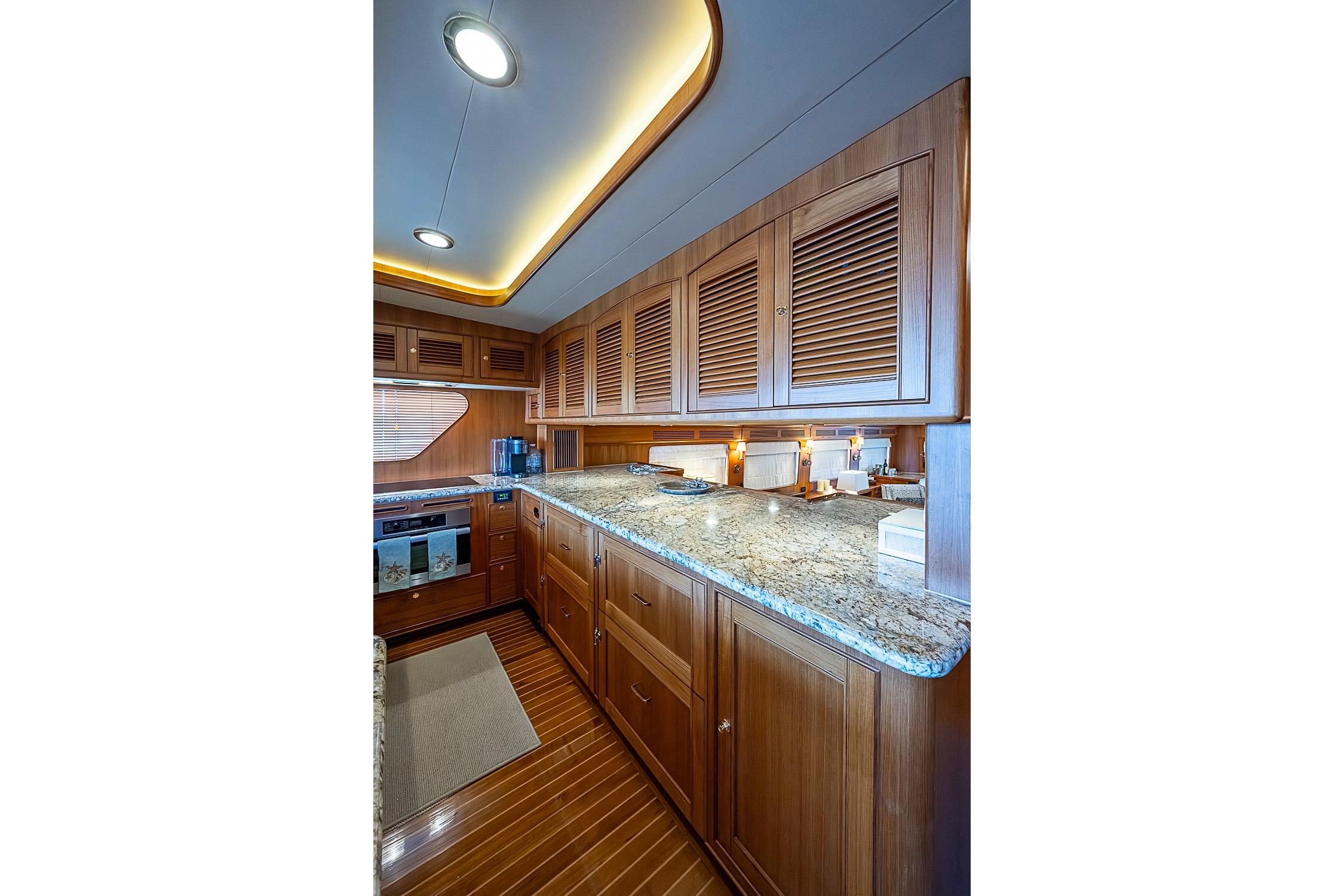 Luxurious kitchen interior of 2014 Marlow 80 Explorer yacht with wooden cabinetry and granite countertops.
