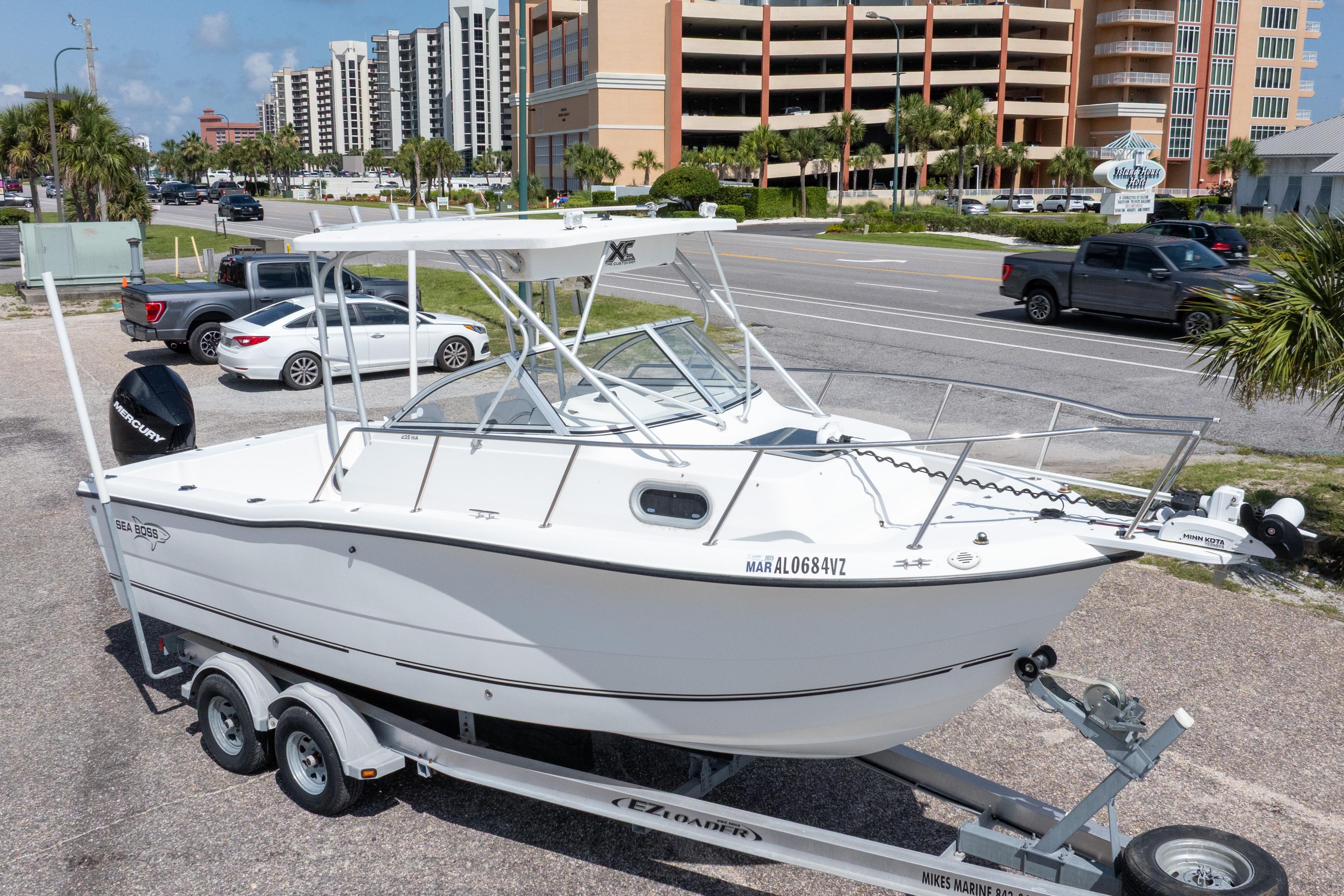2007 Sea Boss 235 Walkaround boat on trailer, parked near coastal buildings and palm trees.