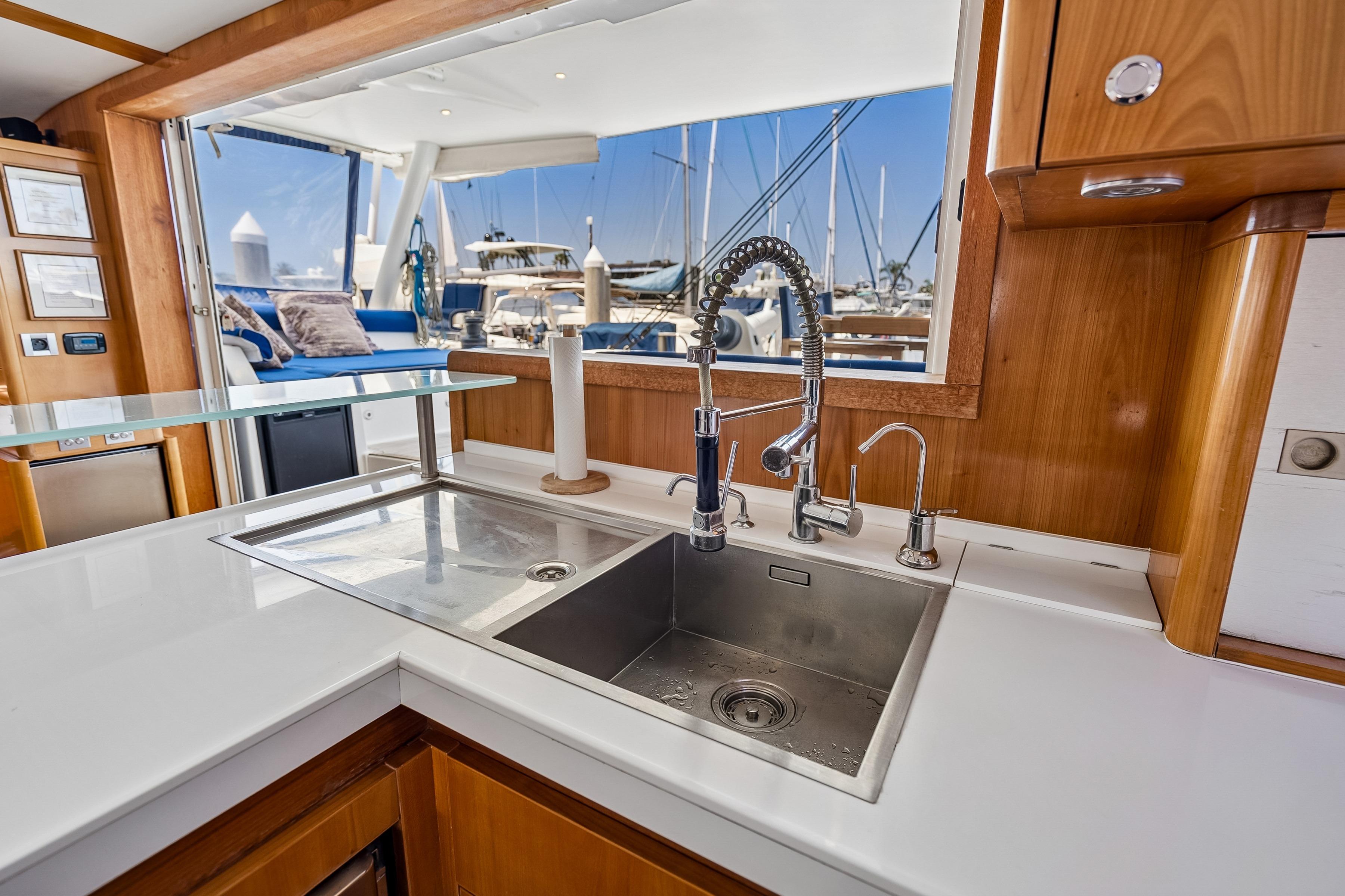 Luxurious Catana 65 yacht kitchen with modern sink, wooden cabinetry, and marina view.
