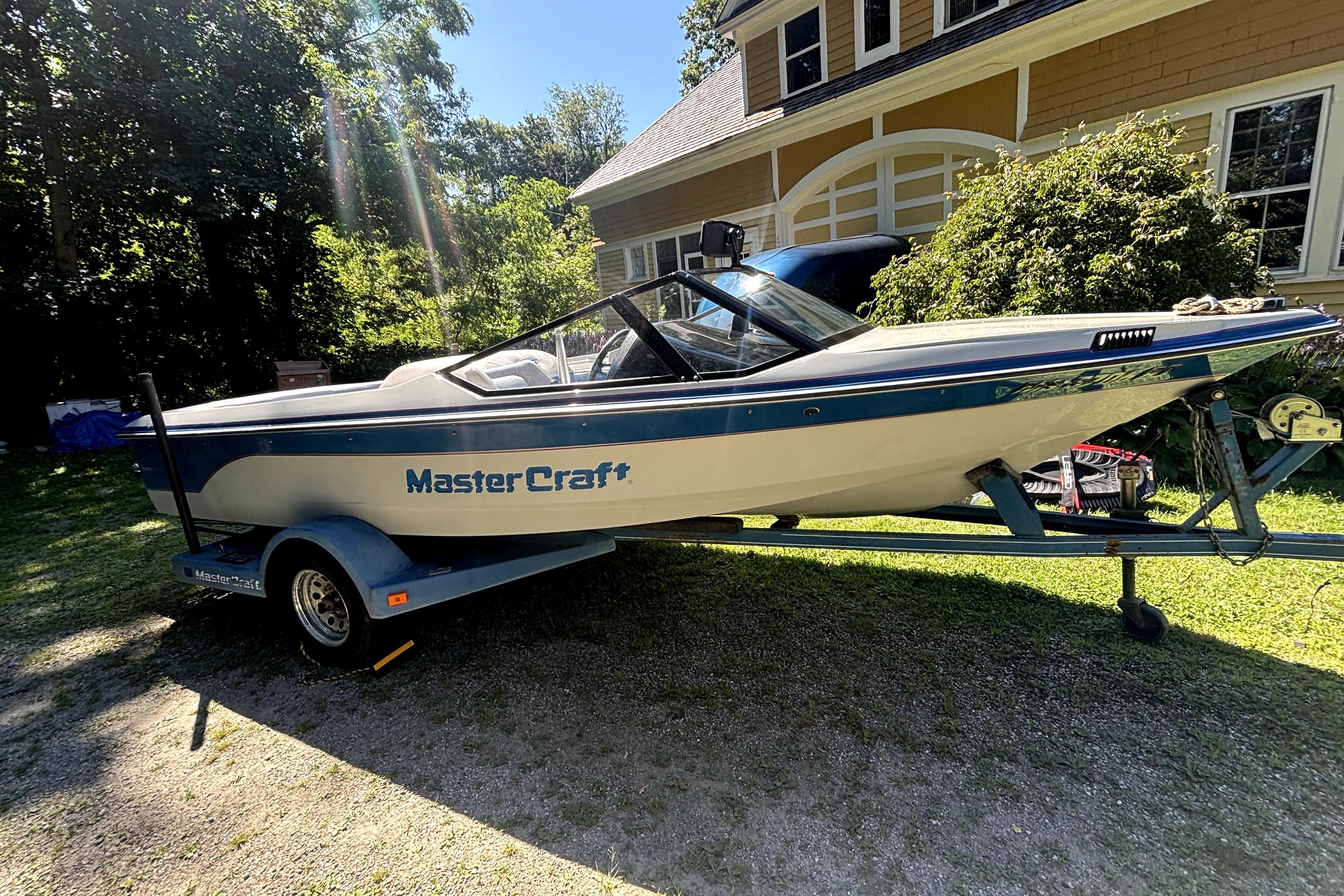 1990 MasterCraft ProStar 190 boat on trailer, parked in a sunny yard near a house.