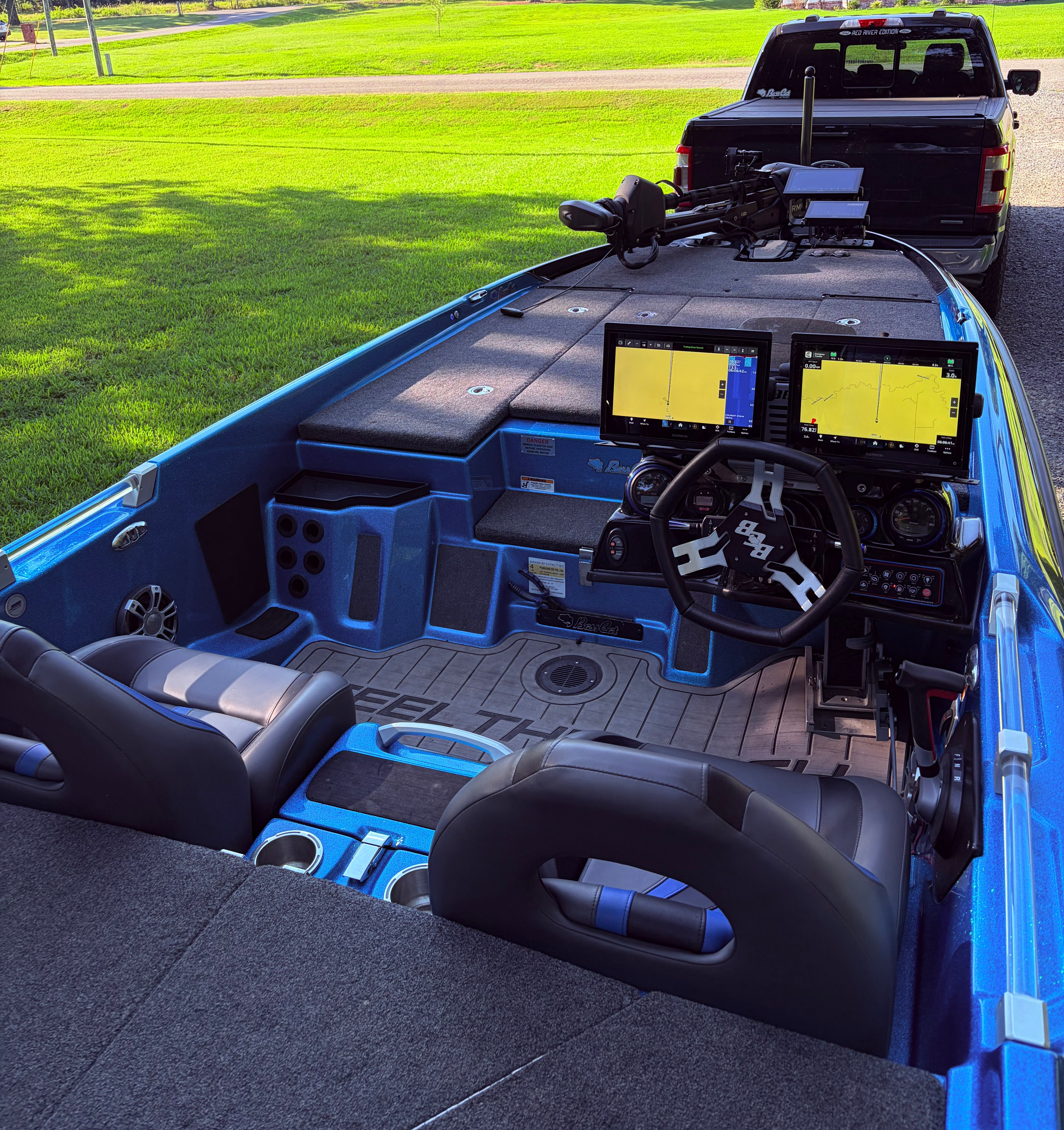 The image shows a blue 2023 Bass Cat Cougar FTD boat. It's hitched to a pickup truck, featuring a modern cockpit with two large screens and two black seats.