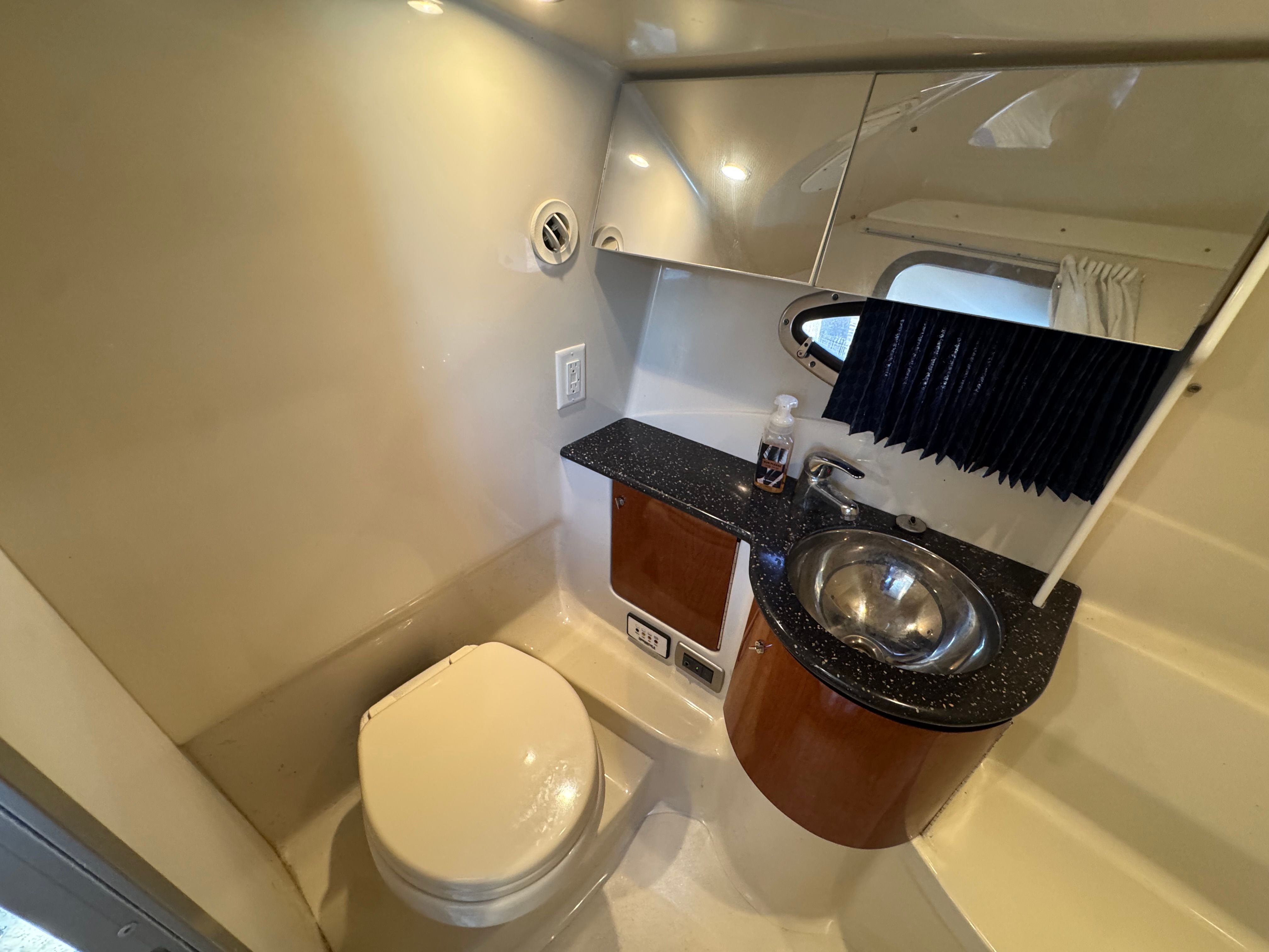 The bathroom of a yacht with a toilet, sink, and mirror.