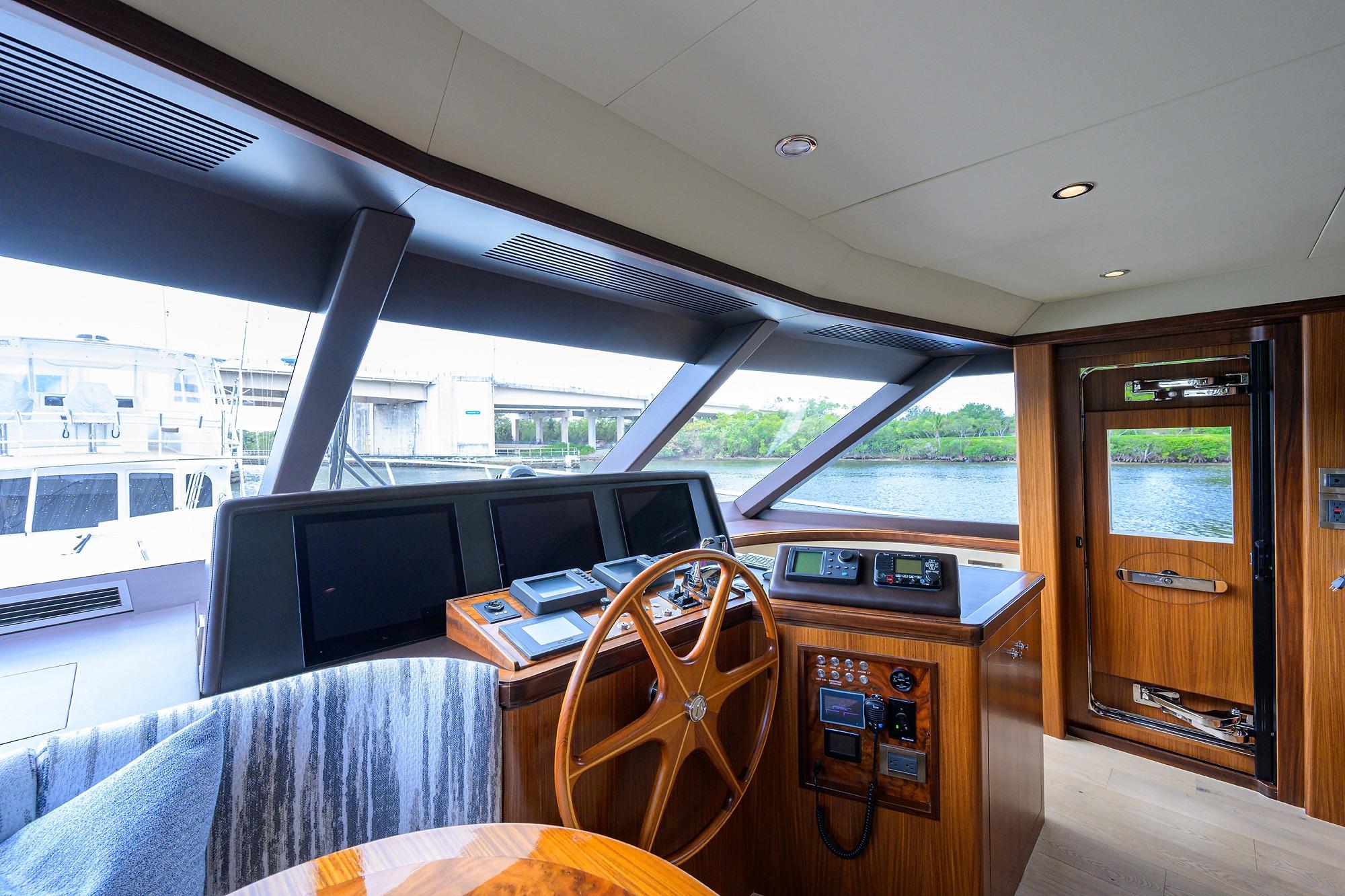 Pilothouse interior of 2016 Ocean Alexander 72, featuring helm with wooden steering wheel and navigation screens.