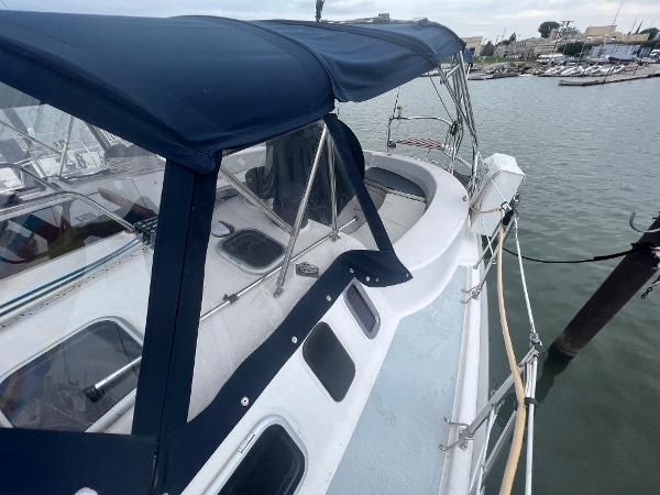 A sailboat with a blue canopy is docked in a harbor. It features a spacious deck.