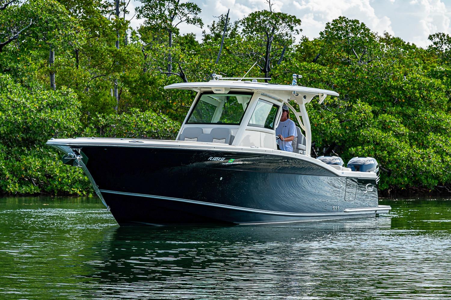 2021 Scout 330 LXF boat cruising on calm water near lush greenery.