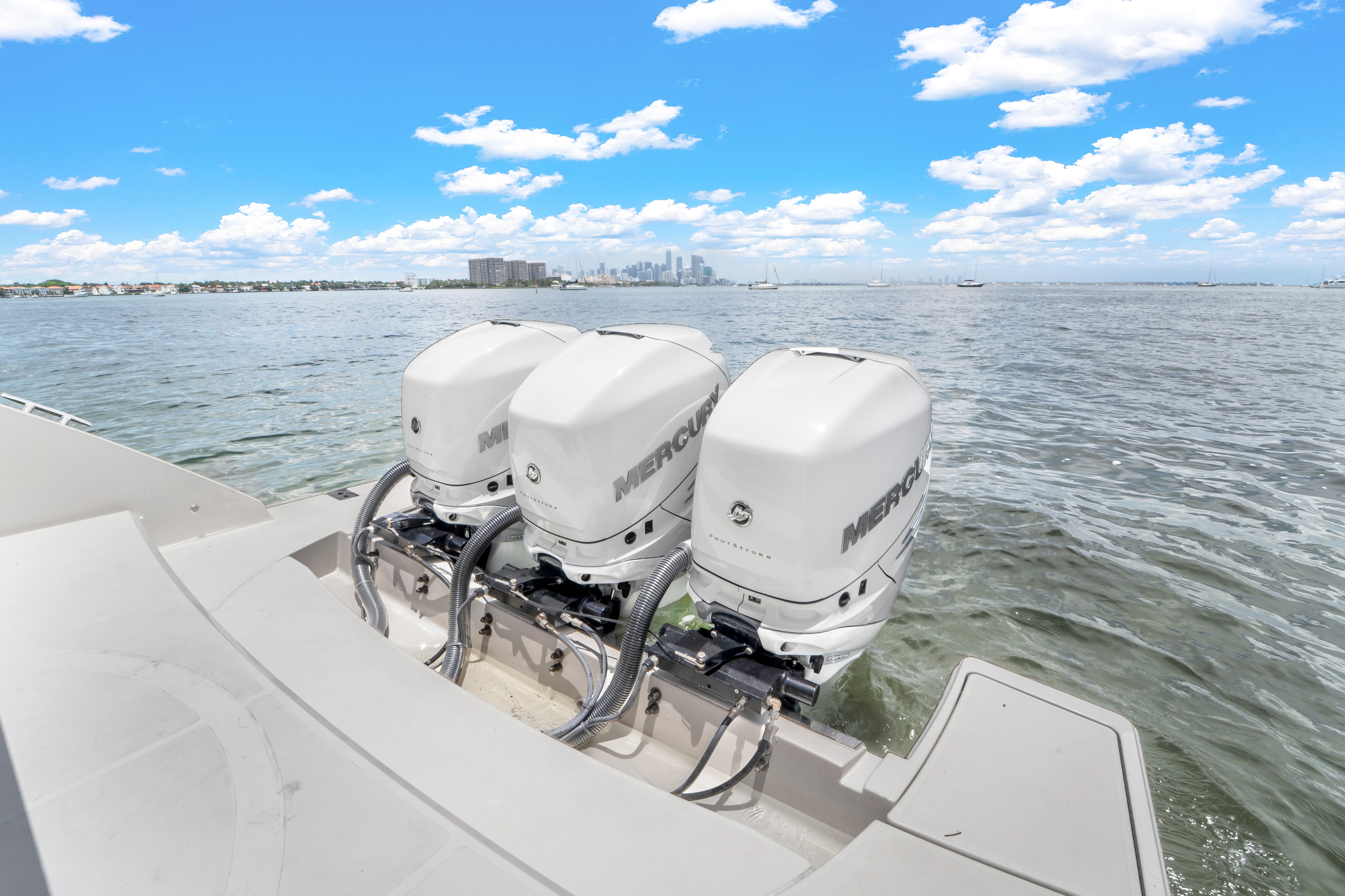 Three Mercury outboard engines on a boat in calm water with a city skyline in the background.