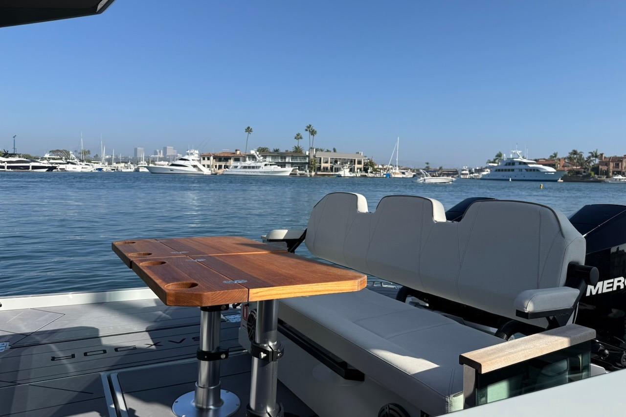 2024 Saxdor 320 GTC boat interior with wooden table, overlooking marina with yachts.
