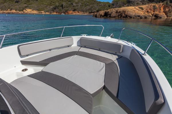 2023 Jeanneau Leader 6.5 CC S3 boat with cushioned seating in a scenic coastal area.