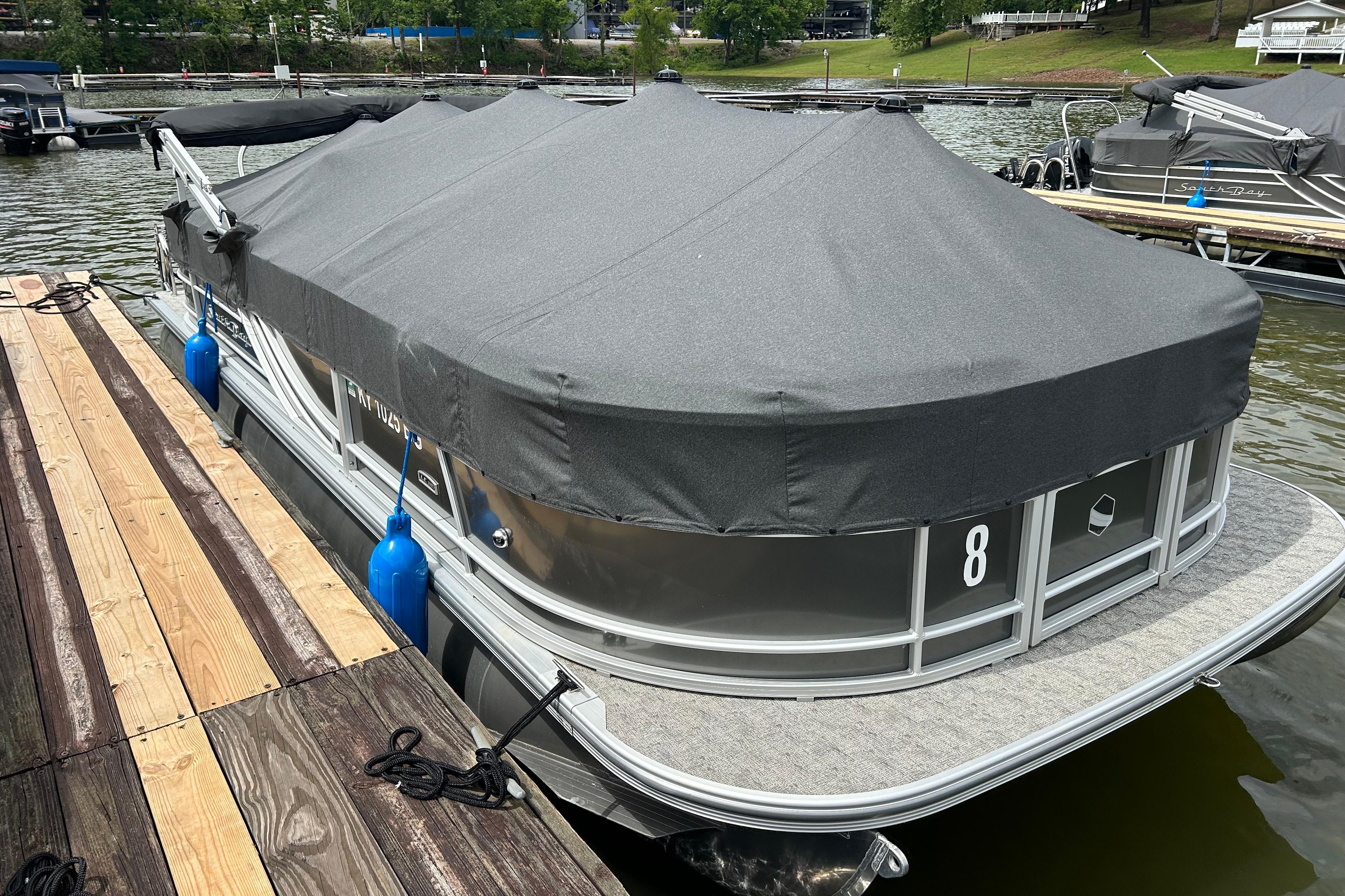 2025 Southbay 224RSLE25 pontoon boat docked with protective cover on a lake.