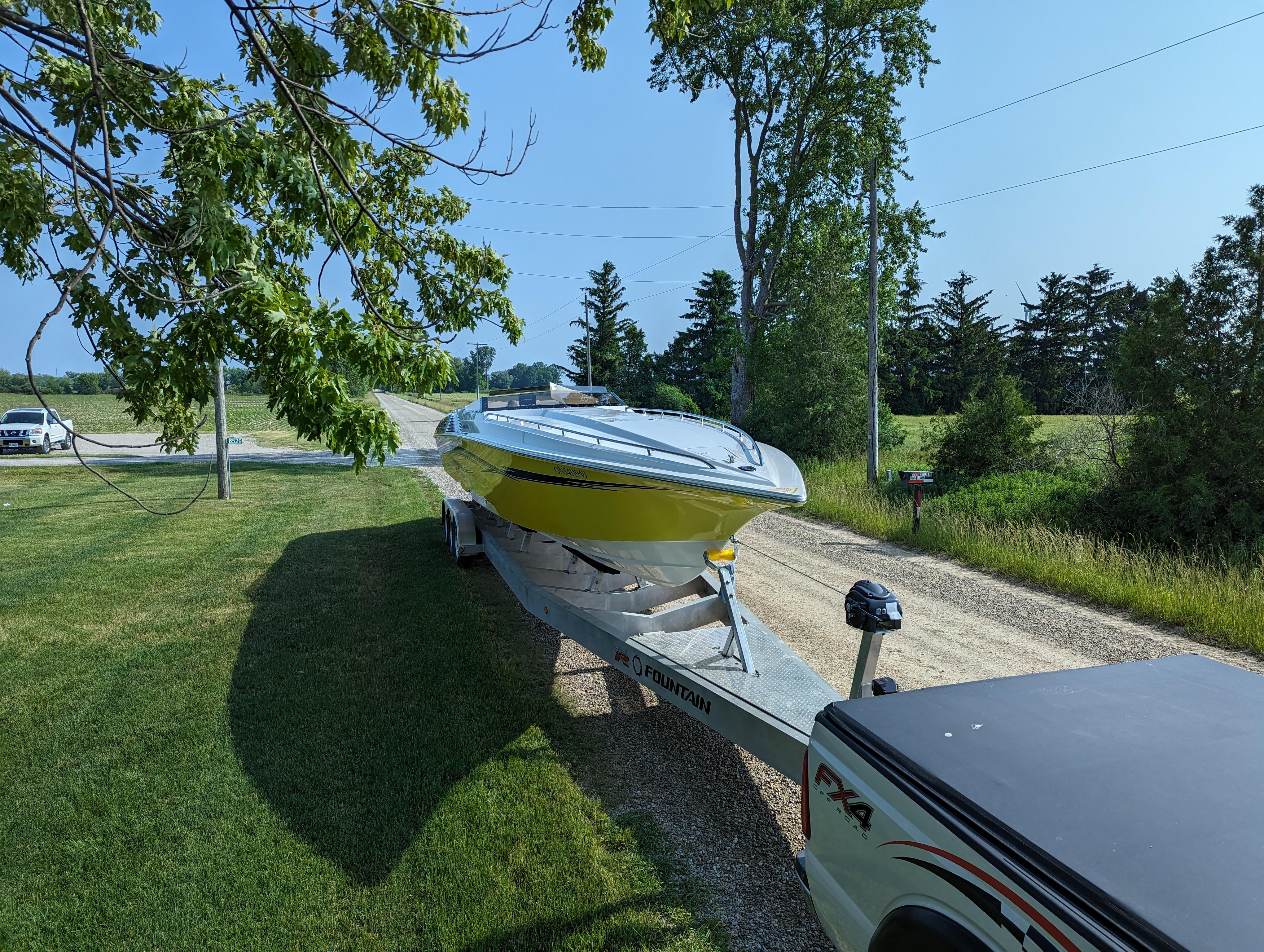 A 2006 Fountain 42 boat on a trailer, parked on a grassy roadside.