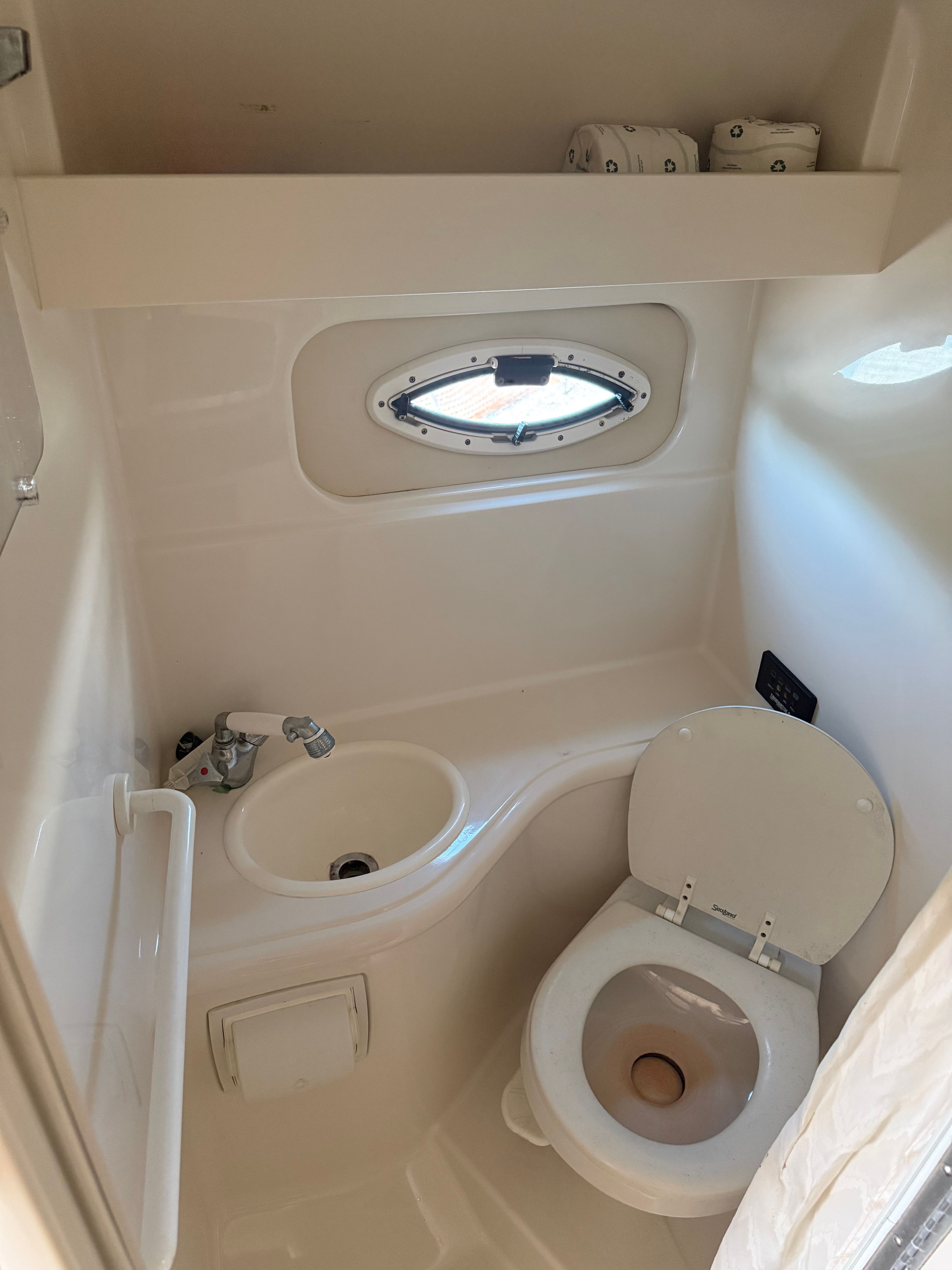 Interior view of a boat bathroom with toilet, sink, and porthole.