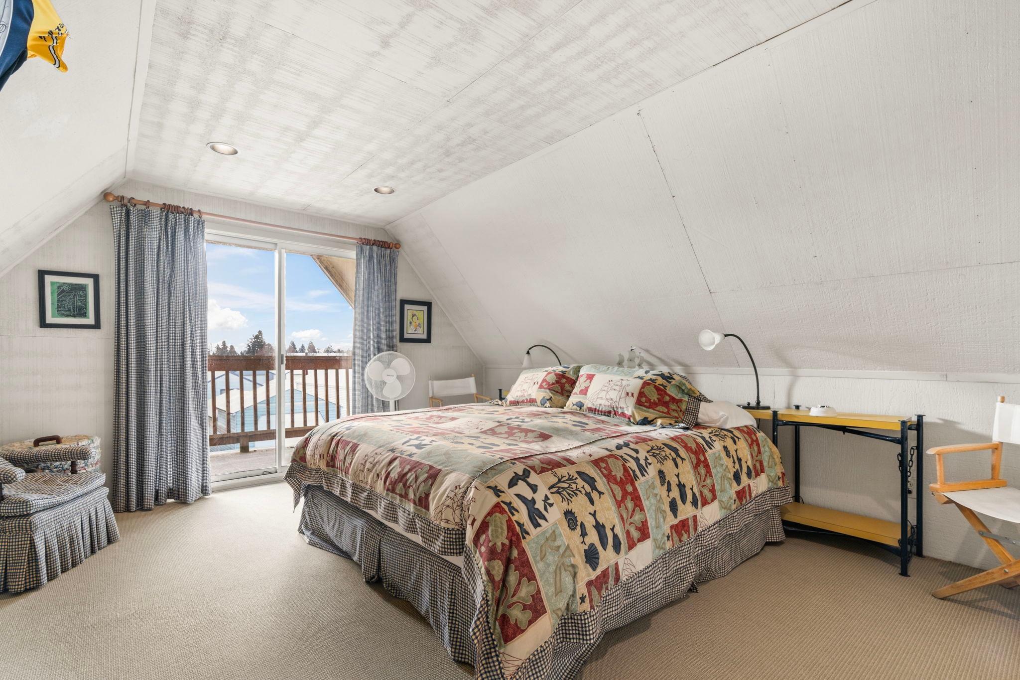 Cozy attic bedroom in 1976 custom boathouse with quilted bedspread and balcony view.