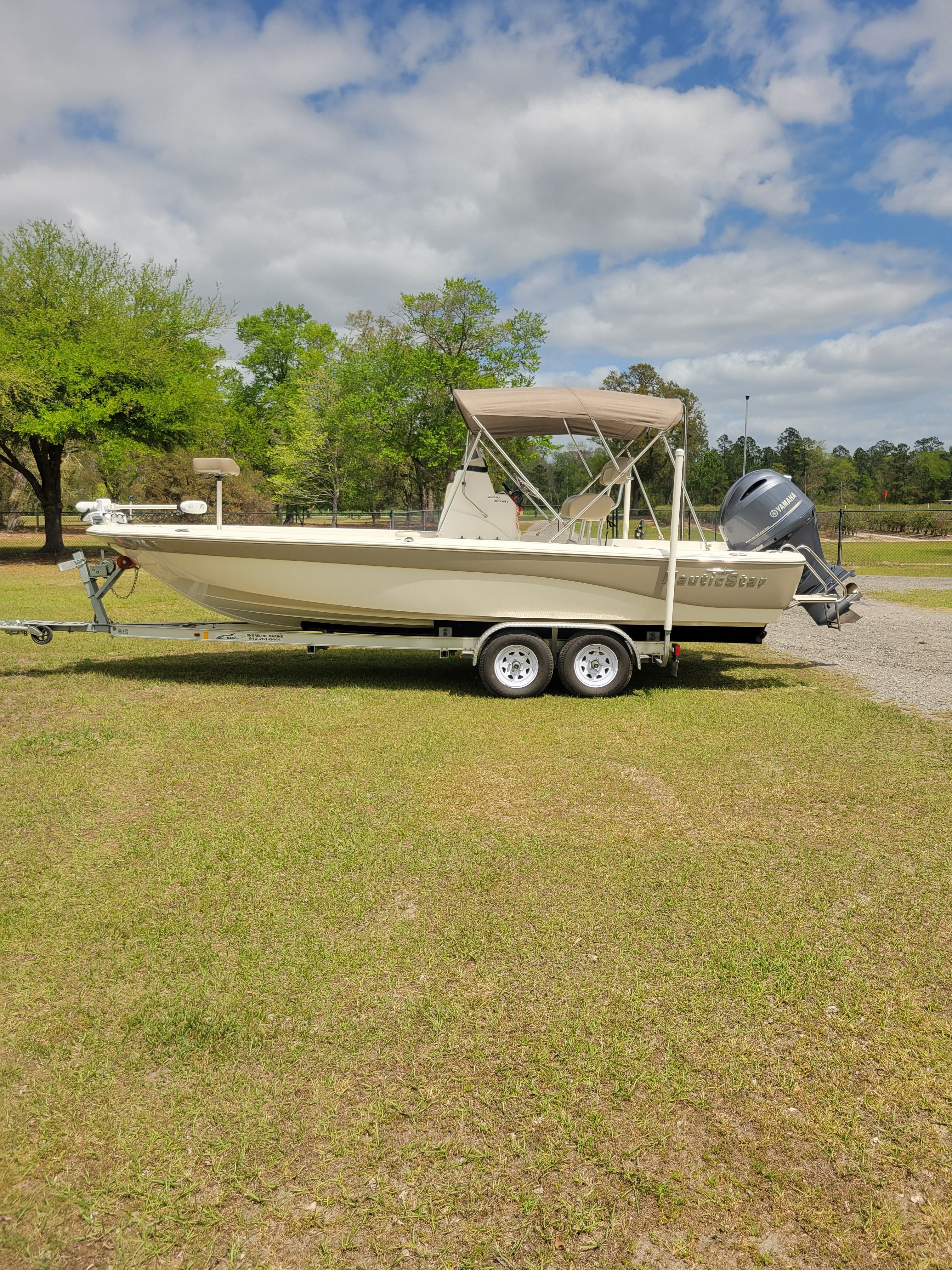 A NauticStar 2200 Sport boat on a trailer on a grassy area.