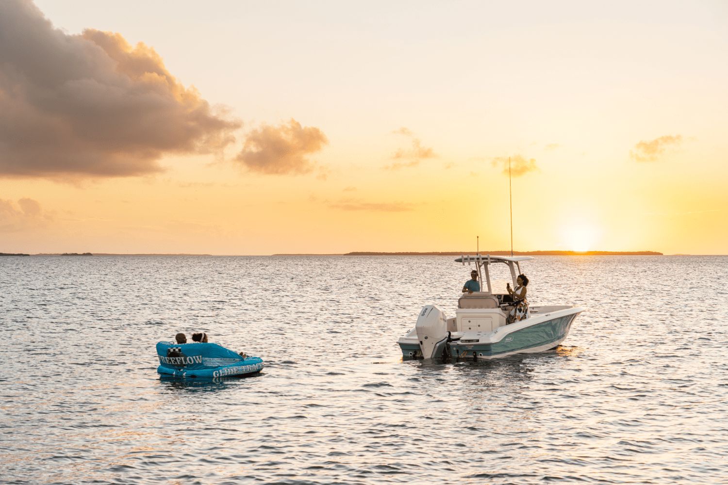 A Boston Whaler 25DA boat on the water at sunset, with a small inflatable nearby.