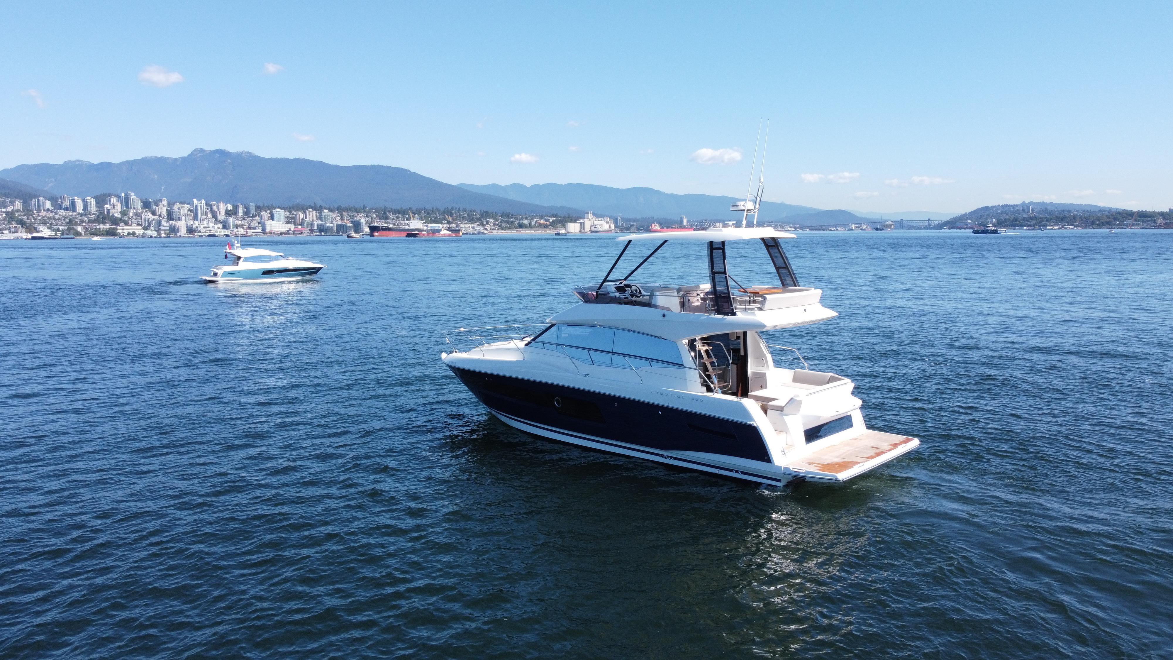 2022 Prestige 460 yacht cruising on a sunny day with cityscape and mountains in the background.