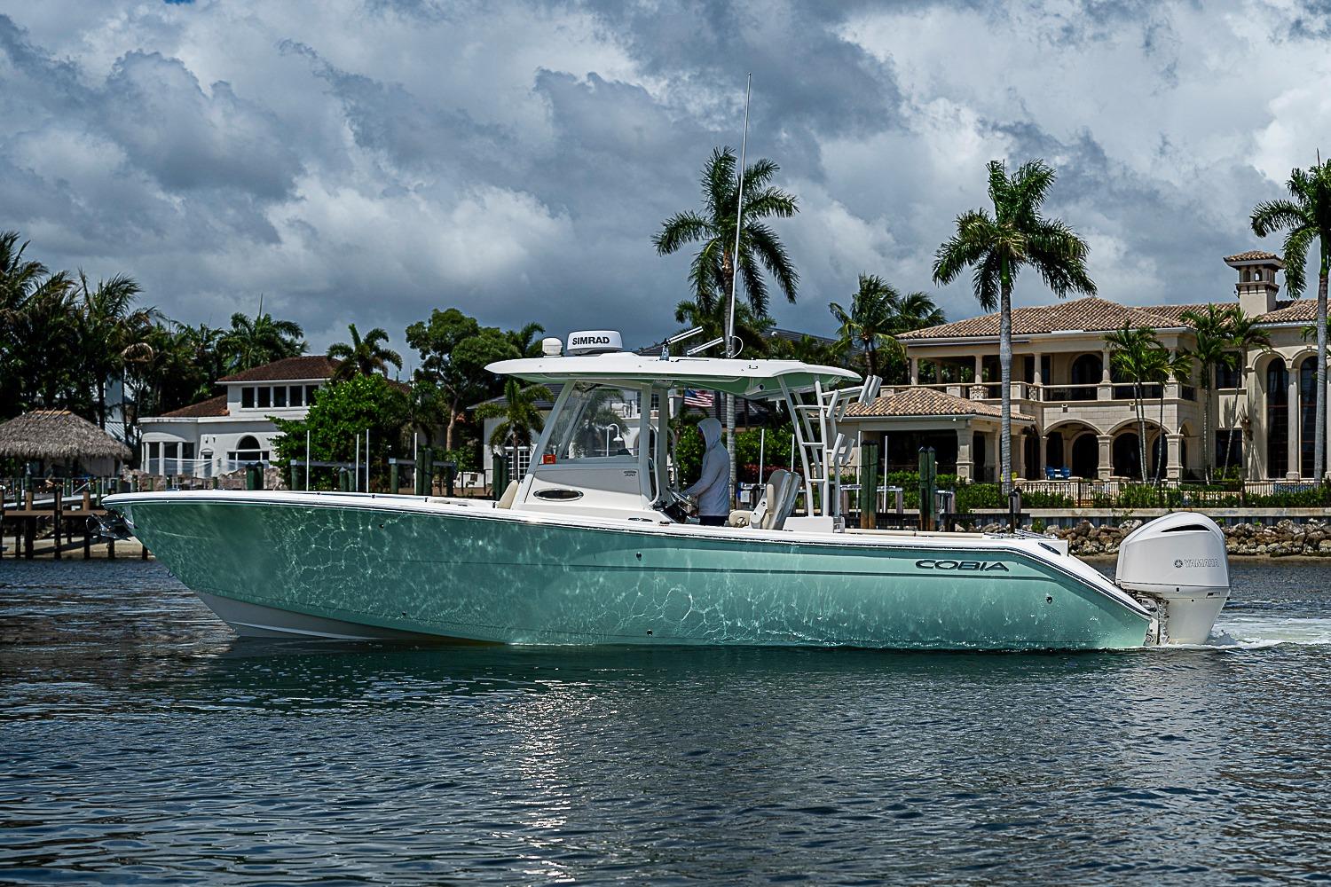 2019 Cobia 320 Center Console boat cruising near luxury waterfront homes.