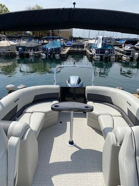 The image shows a pontoon boat with gray seating and a table, docked in a marina.