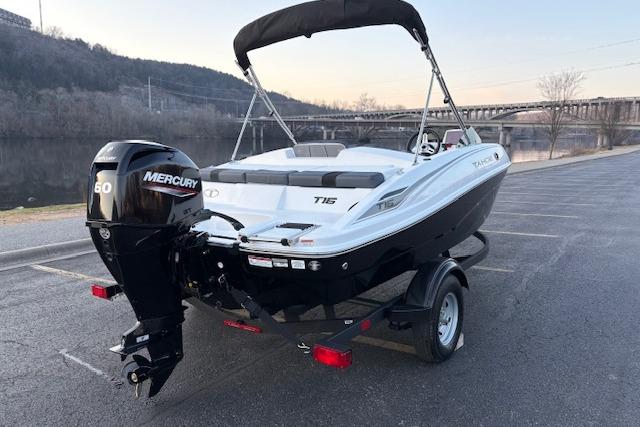2026 Tahoe T16 boat with Mercury engine, parked near a scenic river and bridge.