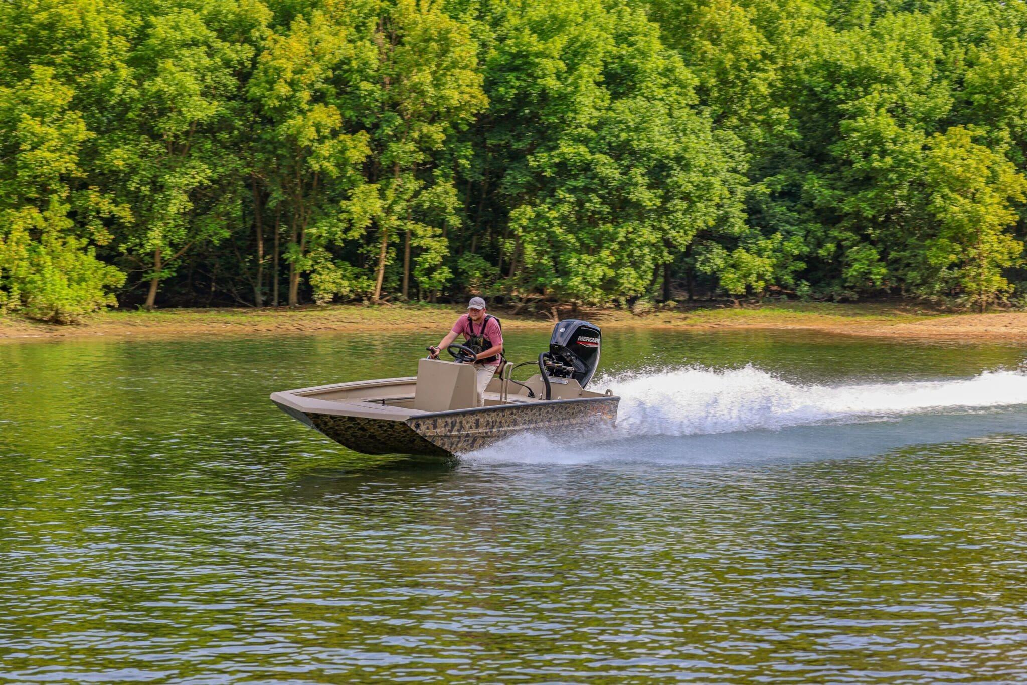 2026 Excel Switchblade boat speeding on a lake with lush green trees in the background.