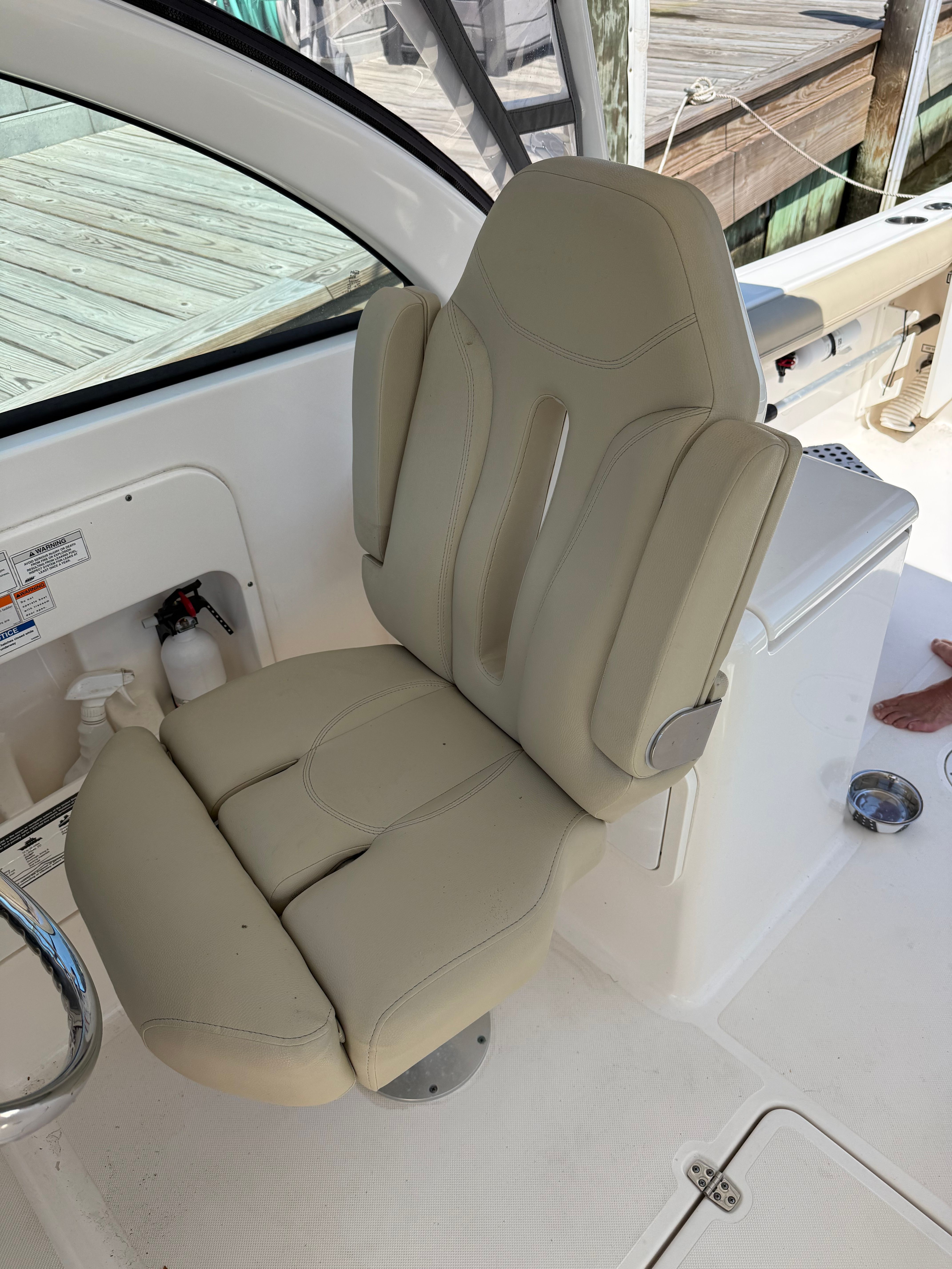A beige captain's chair on a boat with a white deck and wooden dock in the background.