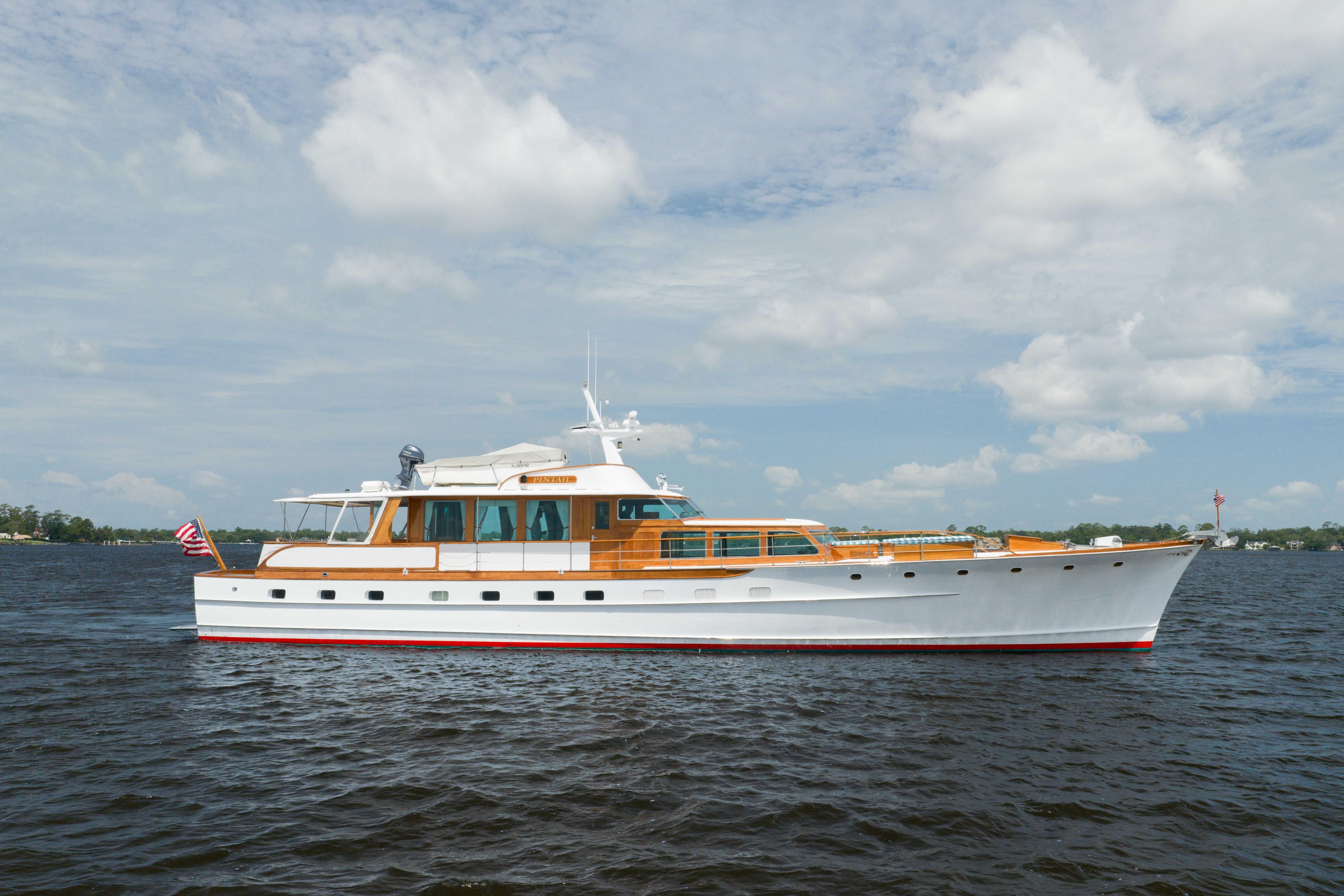 Classic 1963 Trumpy yacht on open water under a partly cloudy sky.