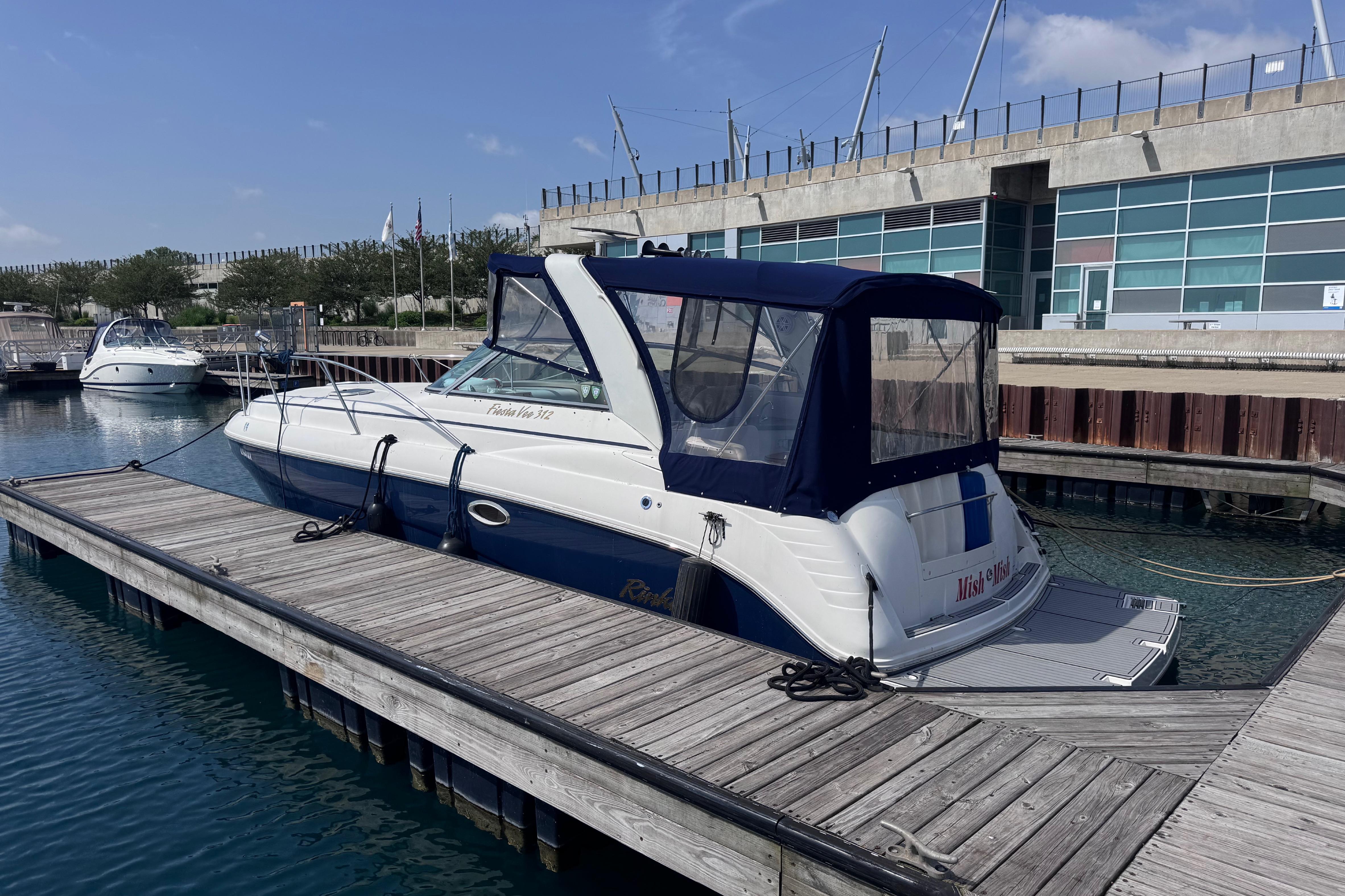 2003 Rinker Fiesta Vee 312 boat docked at a marina with modern building backdrop.