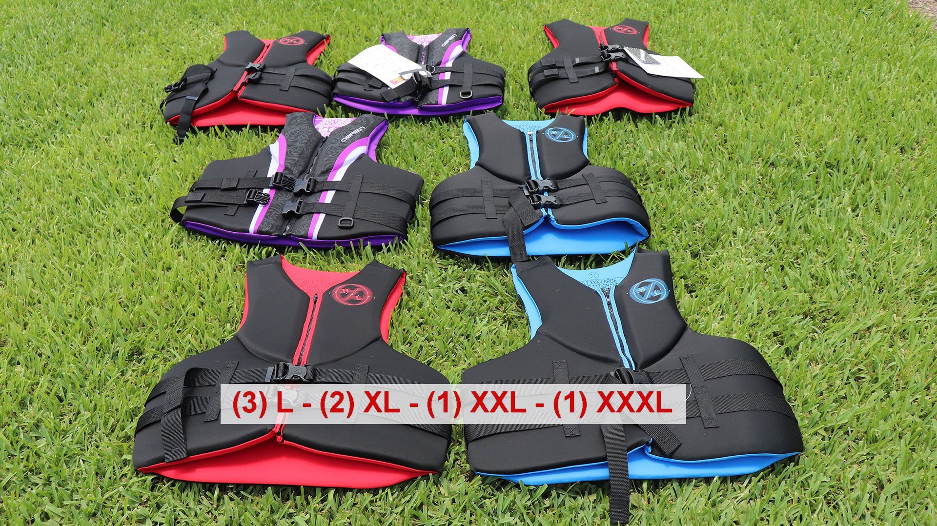 Various life jackets laid out on grass.