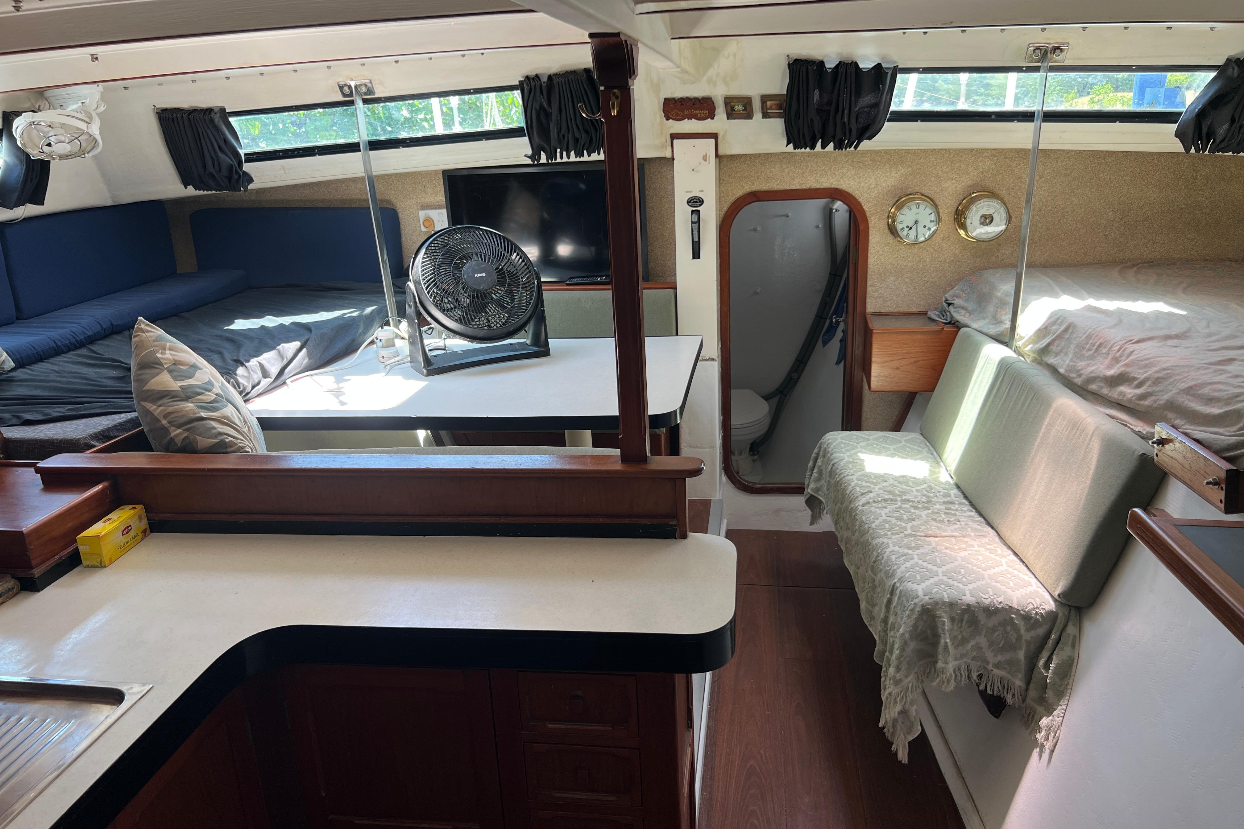 Interior of 1989 Beuhler Custom Trimaran with cozy seating, fan, and nautical decor.