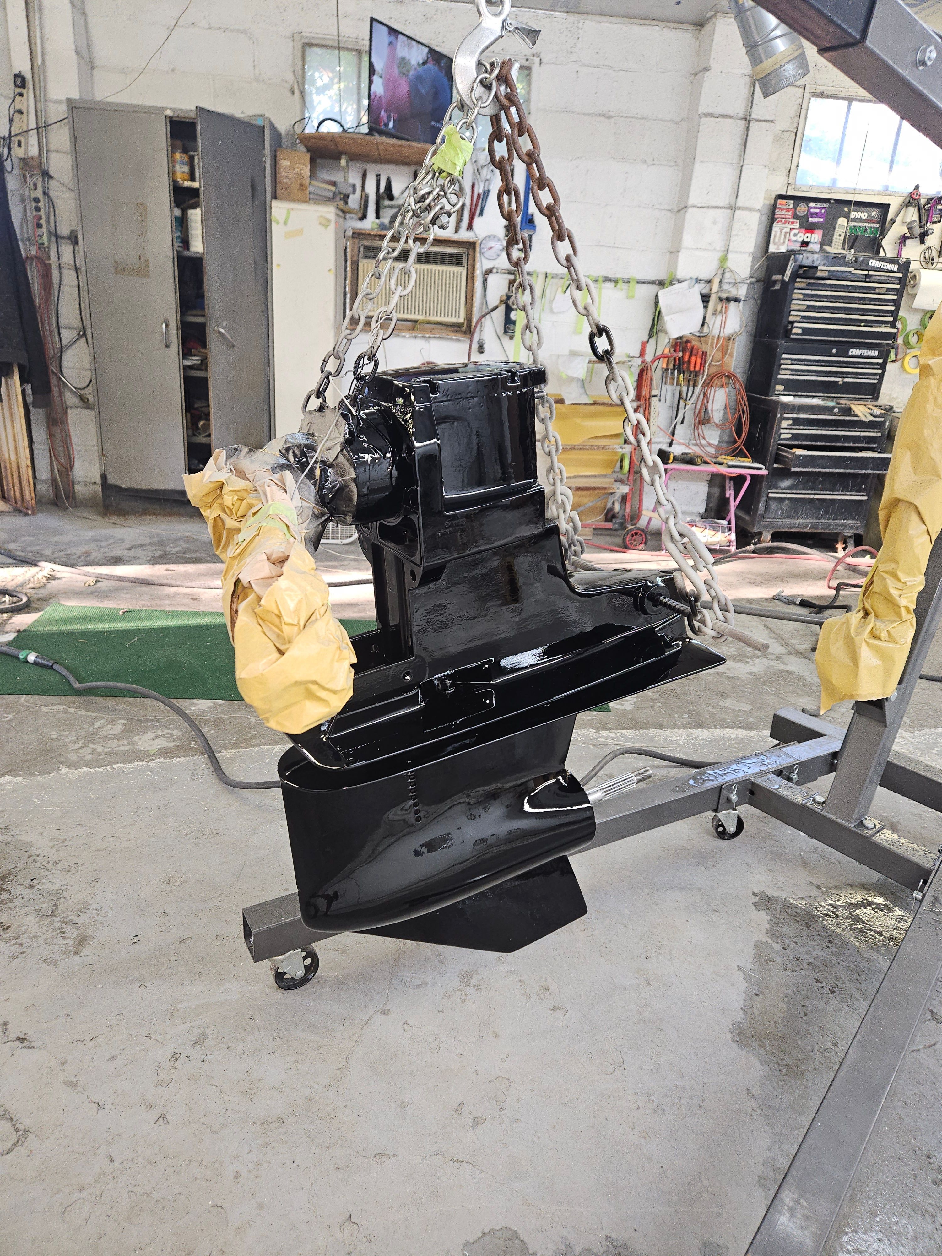 A black boat part hangs from a chain in a workshop.