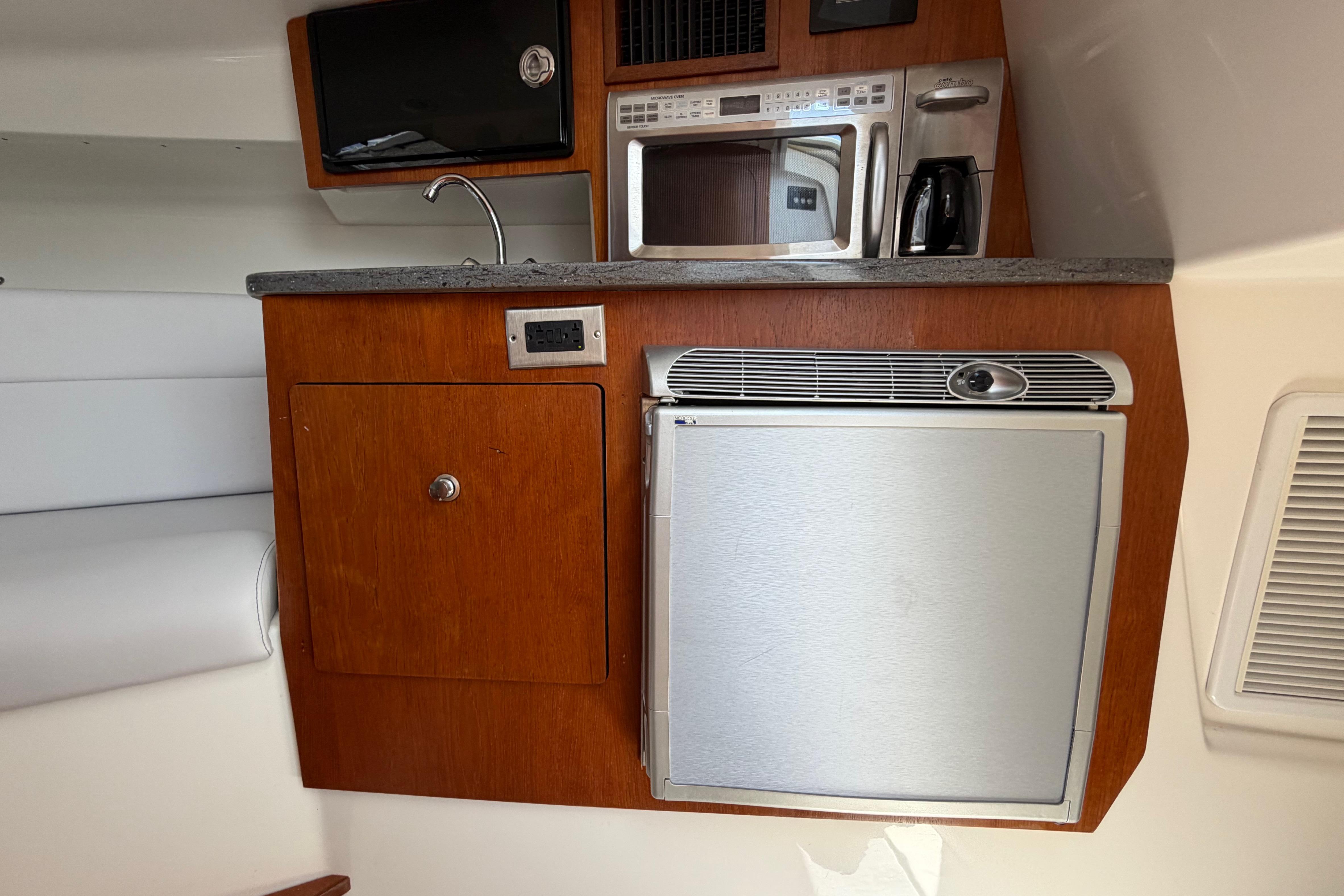 Compact kitchen area in a 2009 Everglades 350LX boat with microwave and fridge.