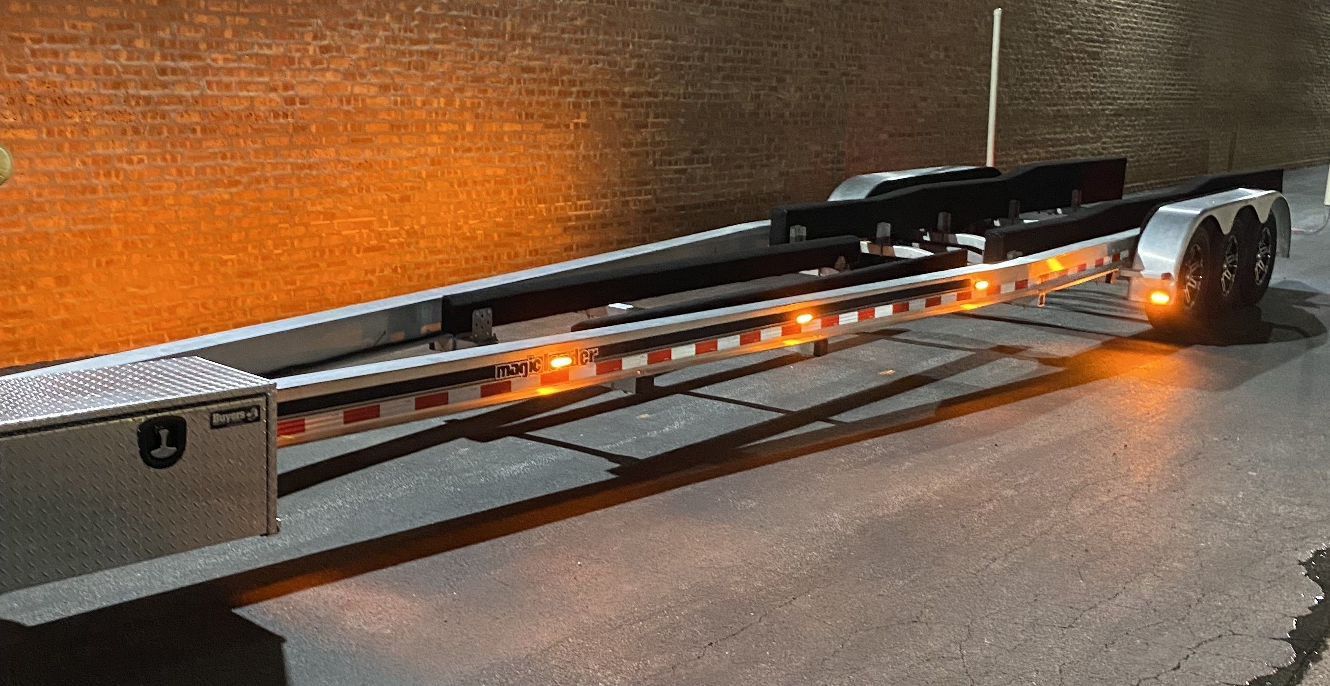 A boat trailer is parked on a paved surface next to a brick wall.