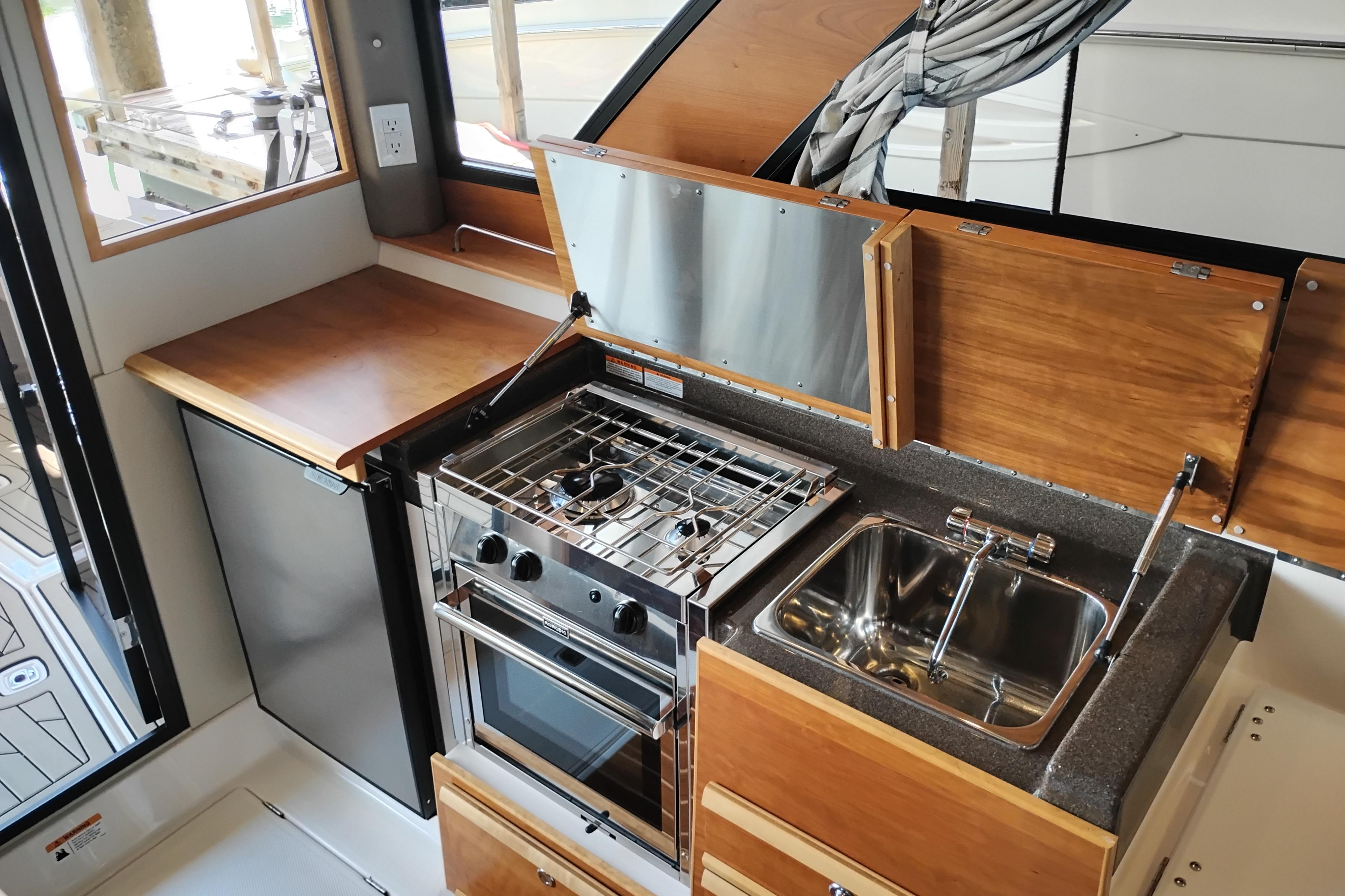 2022 Cutwater C-32 Coupe kitchen with stove, sink, and wooden cabinetry.