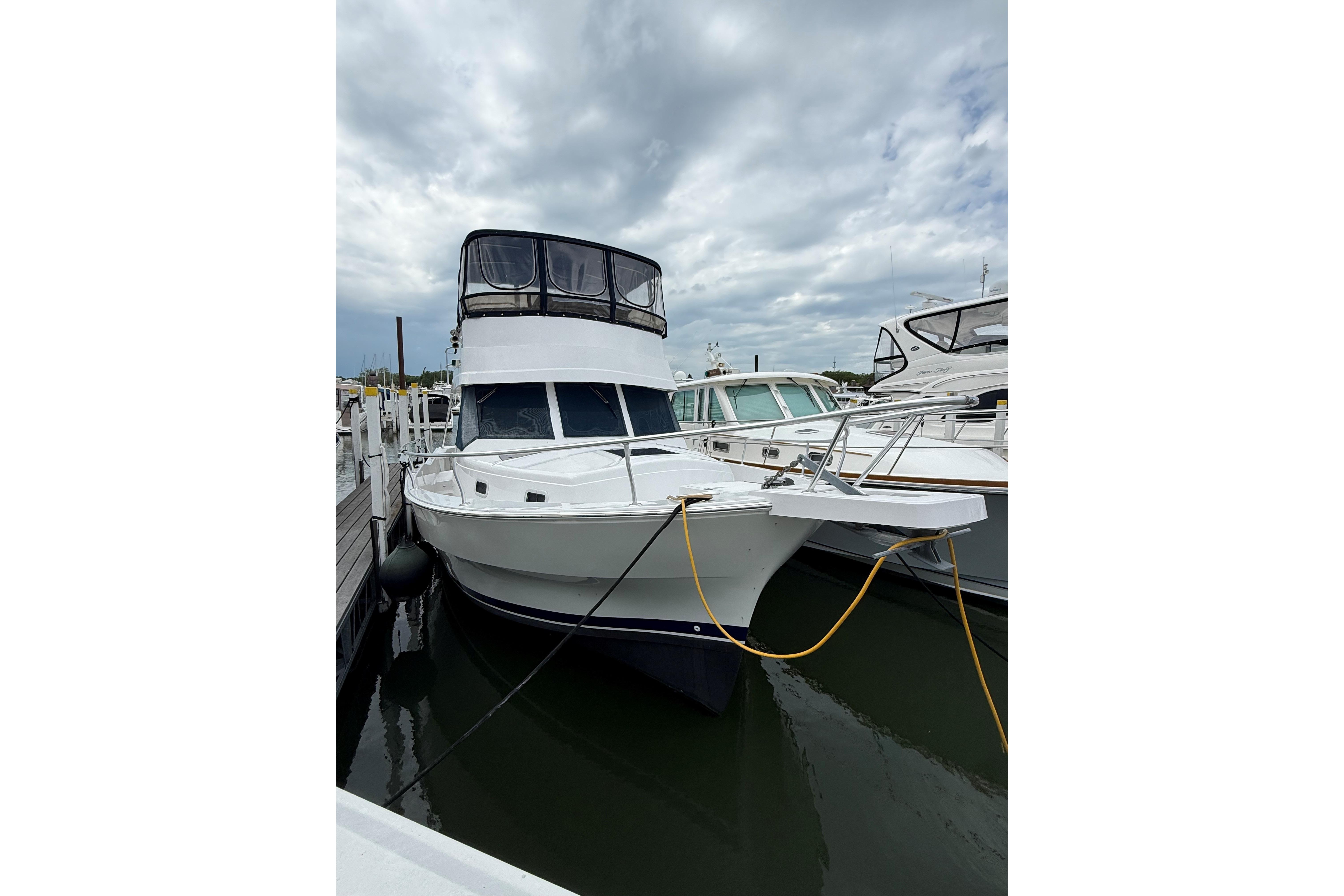 1999 Mainship 350 Trawler docked at marina under cloudy sky.