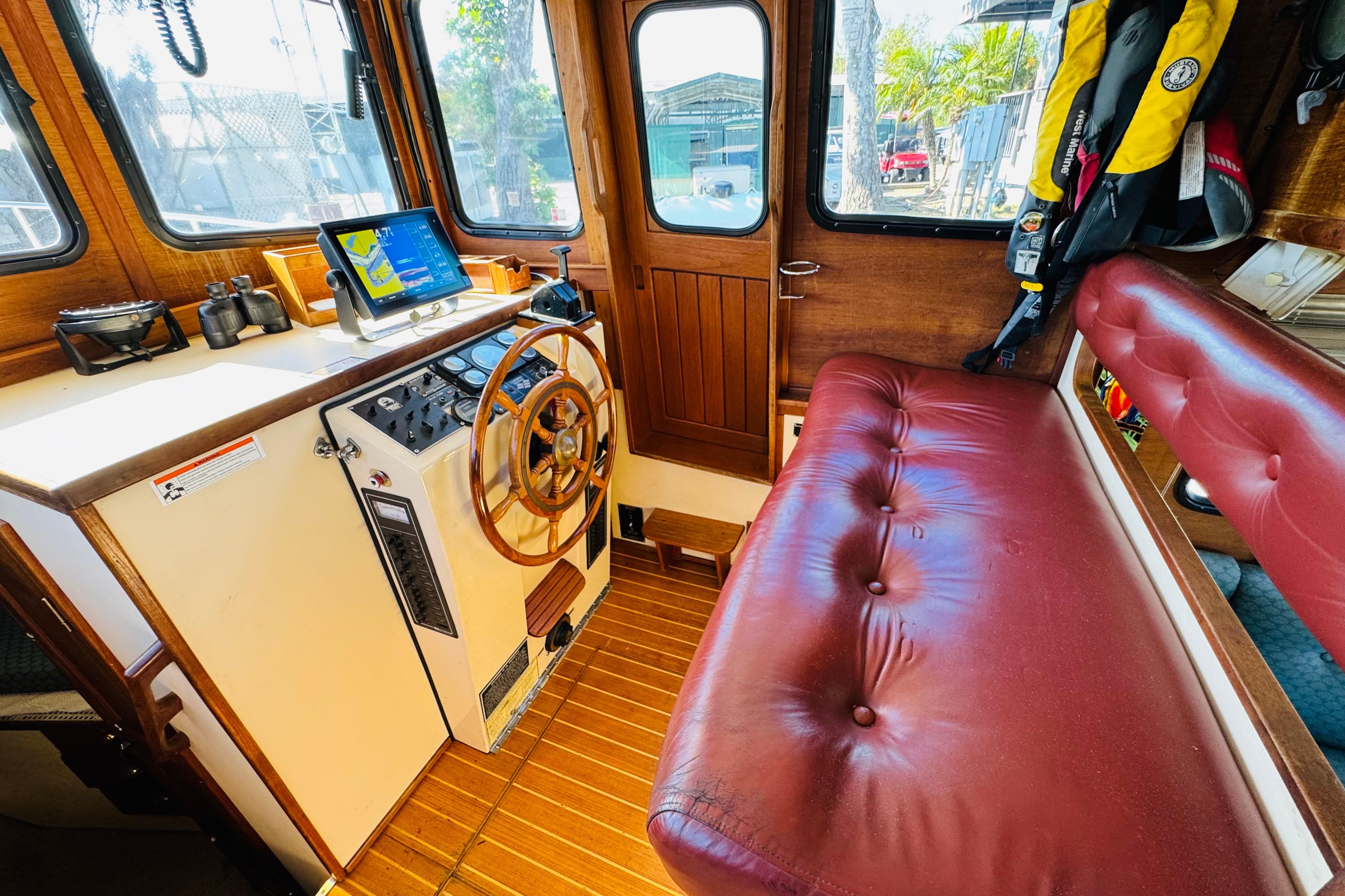 Interior of a 1996 Nordic Tug 32 with wooden helm, red seating, and navigation equipment.