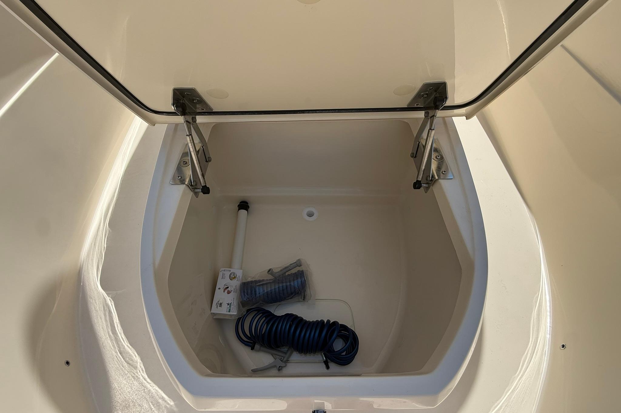 Open storage compartment in 2027 Scout 240 XSF boat, featuring coiled hose and accessories.