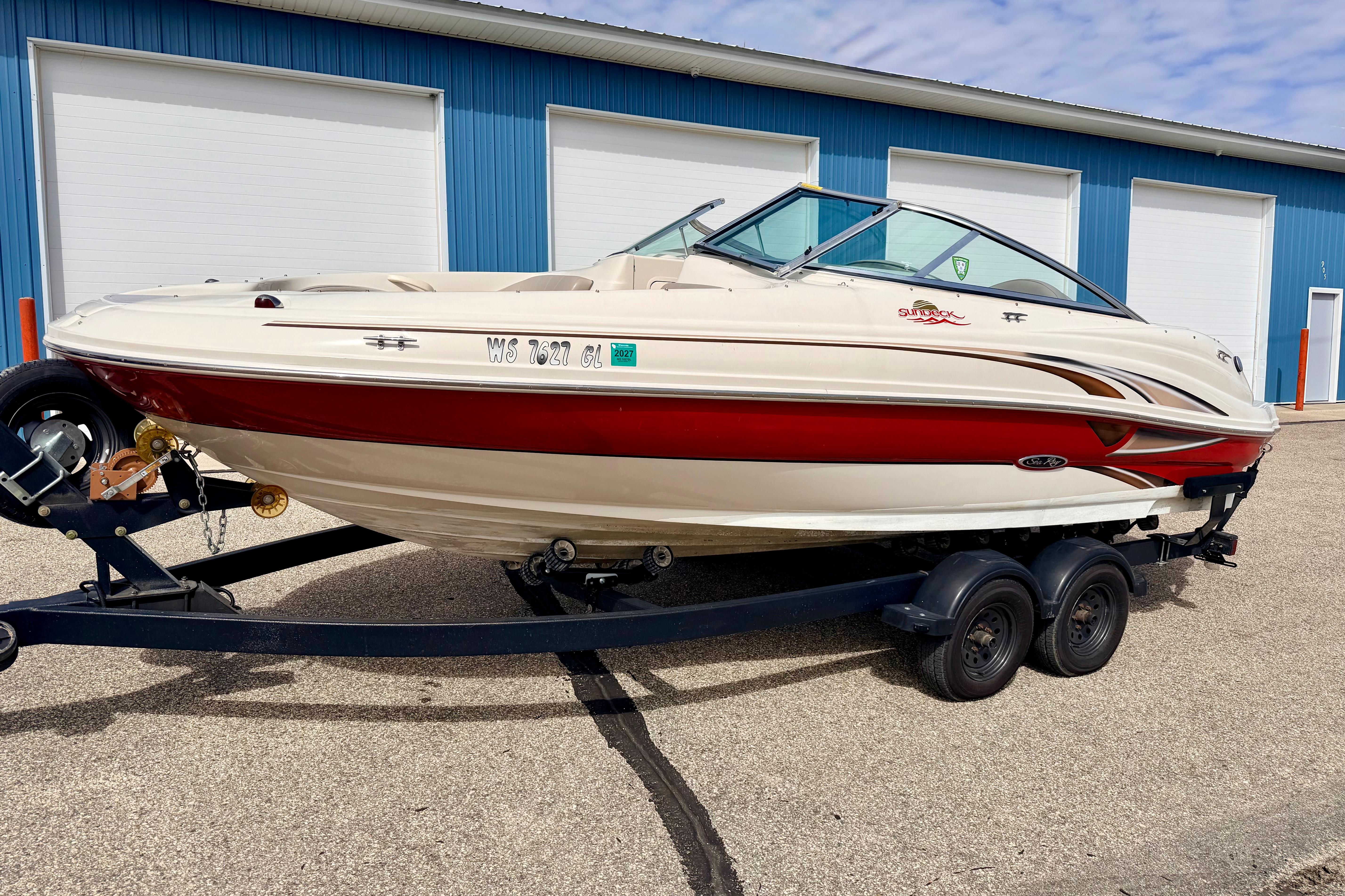 2003 Sea Ray 200 Sundeck boat on trailer, parked outside blue warehouse.