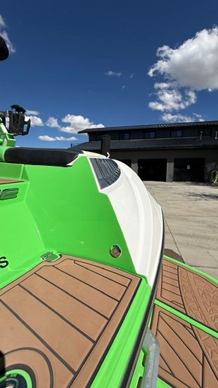 A bright green boat with a brown deck is on a concrete lot in front of a modern building.