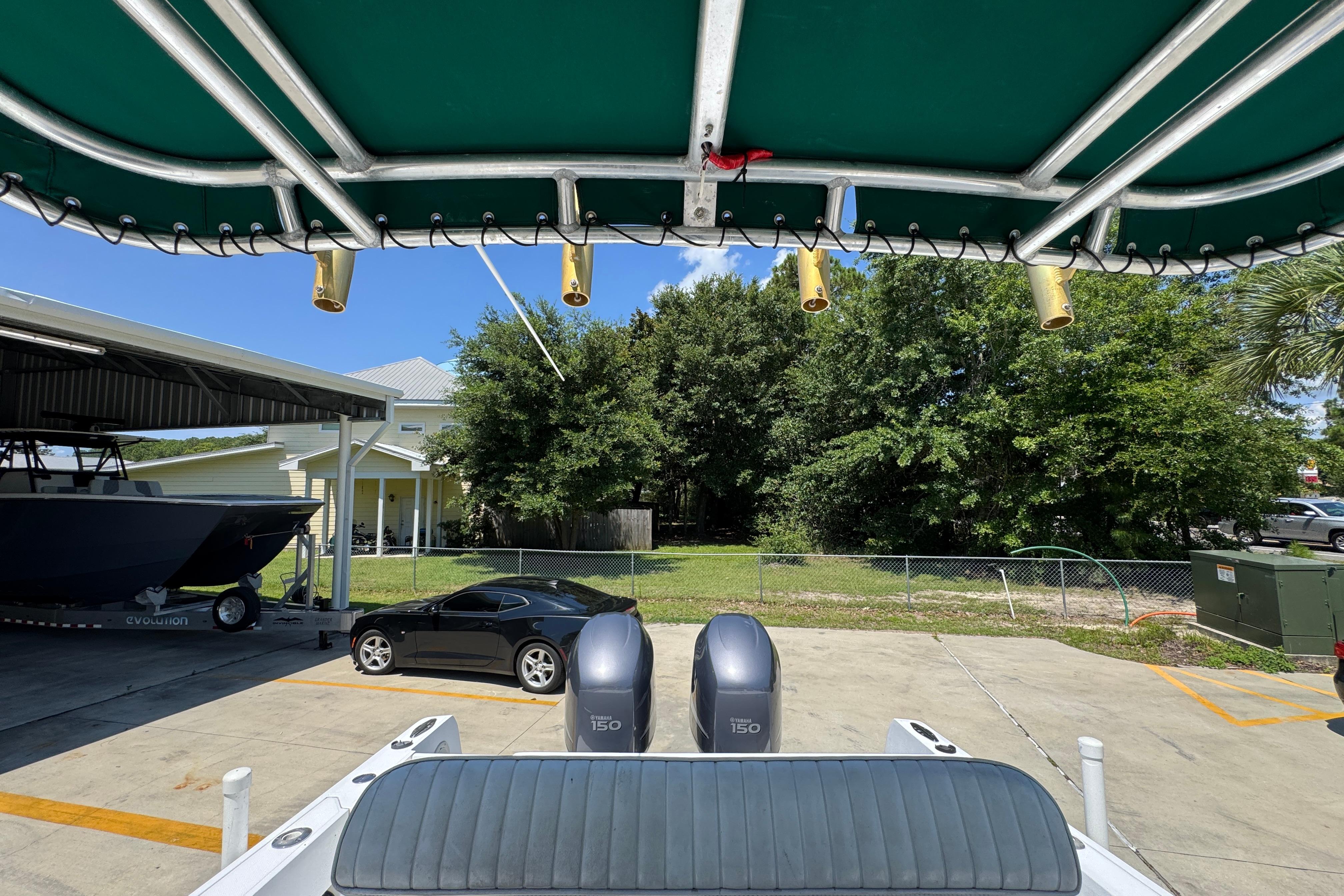 2000 Stamas 250 Tarpon boat with dual engines, parked near a black car and trees.