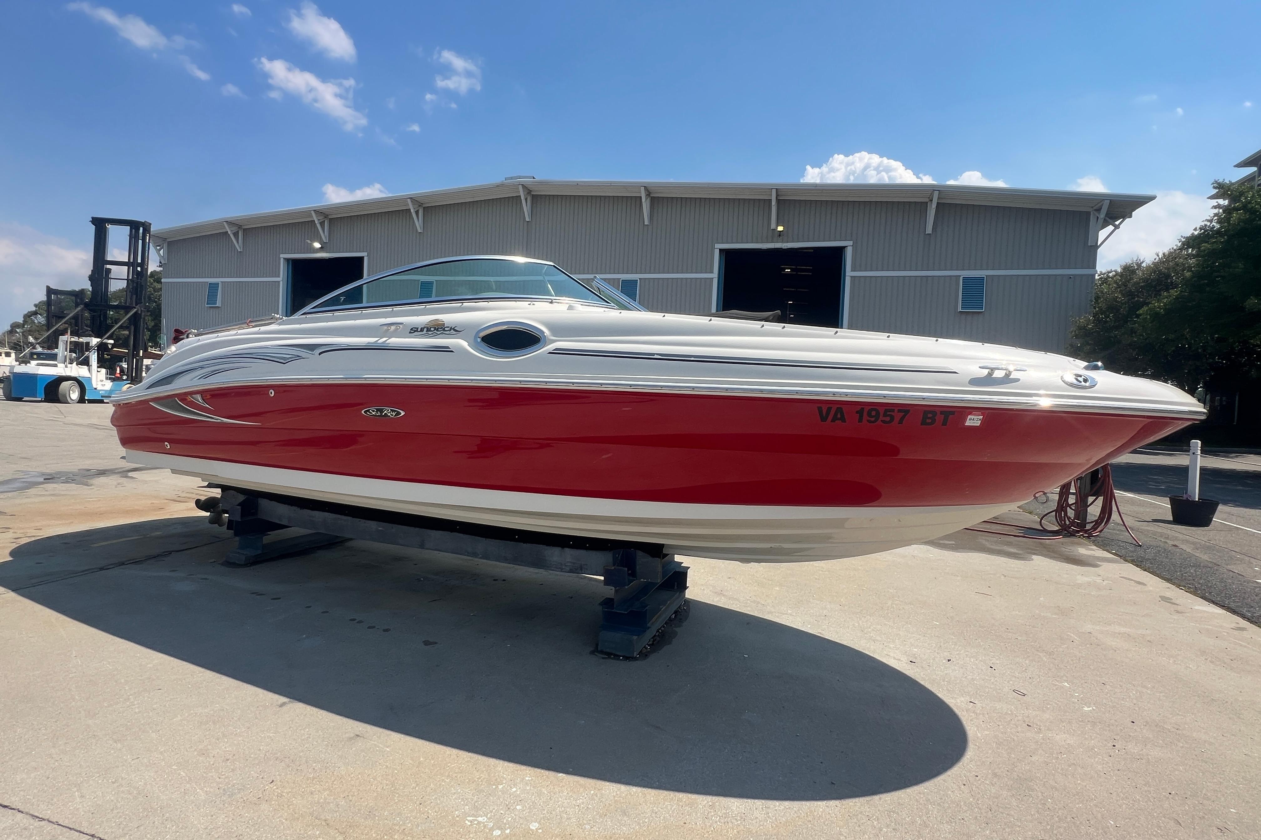 2005 Sea Ray 240 Sundeck boat with red hull, displayed outdoors on a stand.