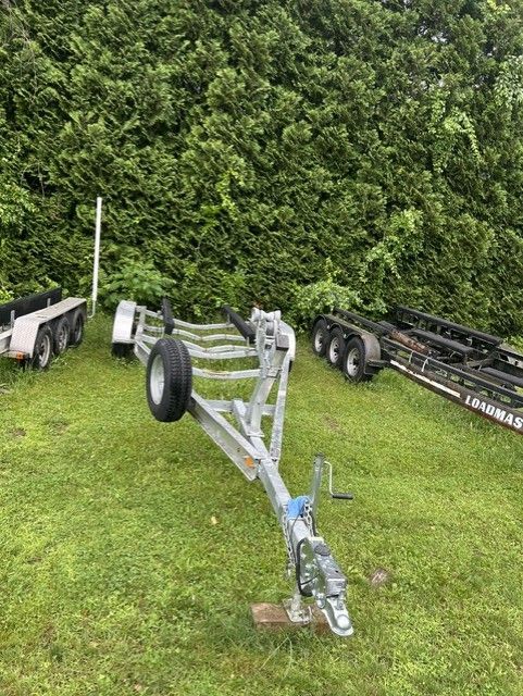 A boat trailer sits on a grassy area, surrounded by trees and other trailers.