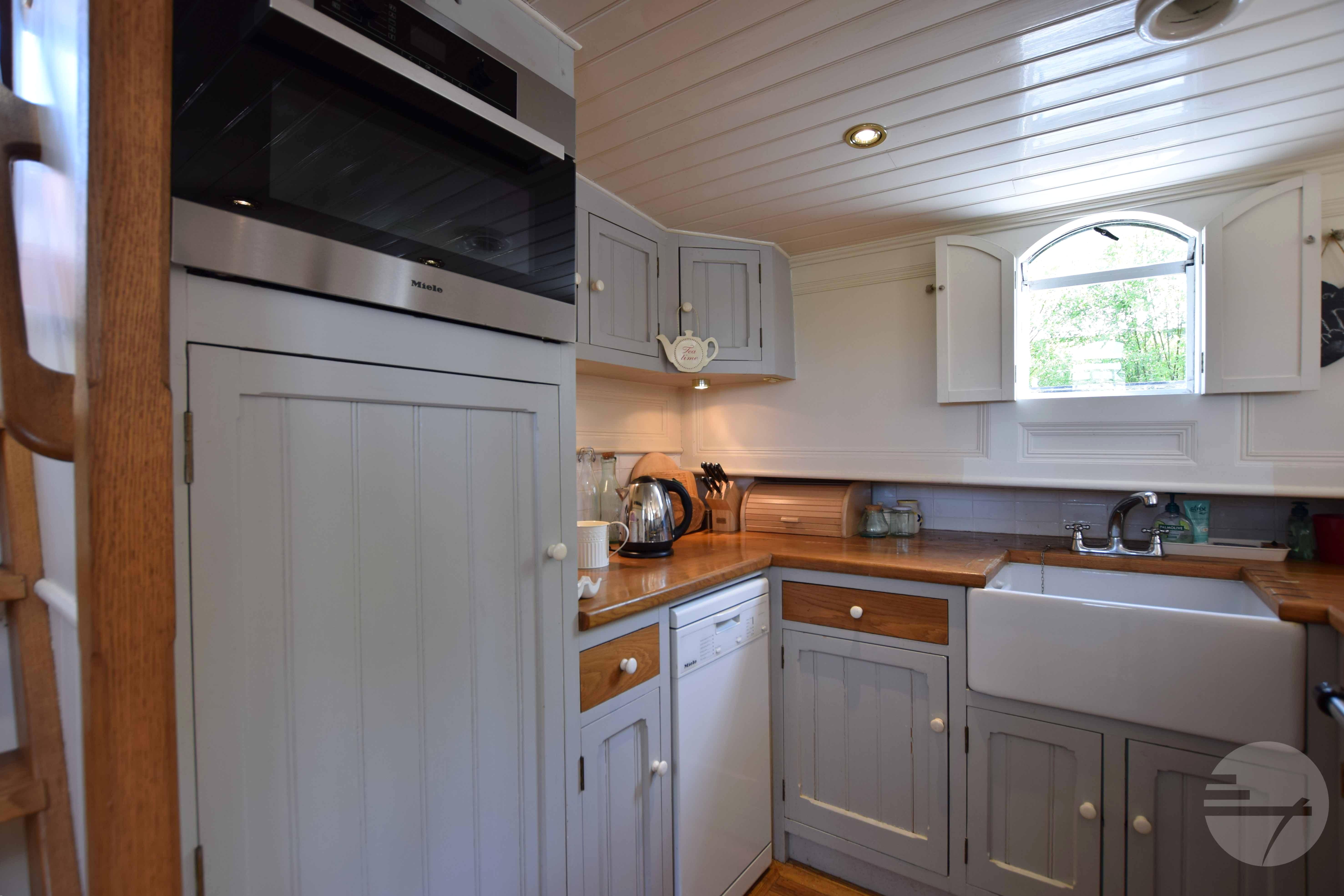 Cozy kitchen in 2010 Custom Dutch Barge Replica with wooden cabinets and farmhouse sink.