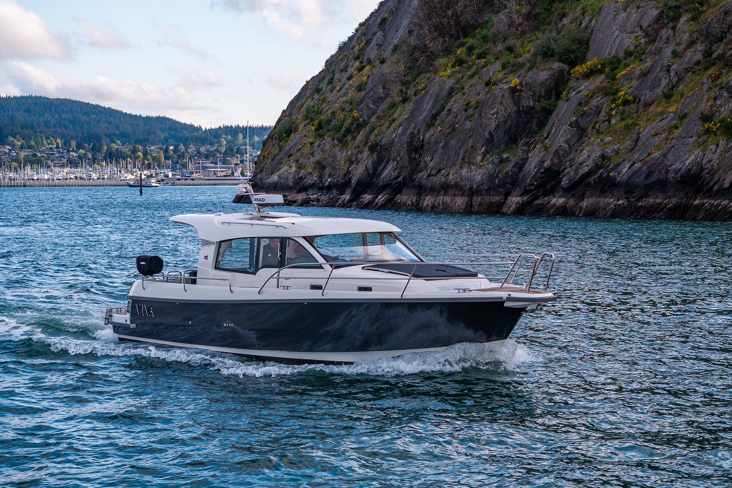 2022 Nimbus 365 Coupe cruising near rocky coastline with marina in background.