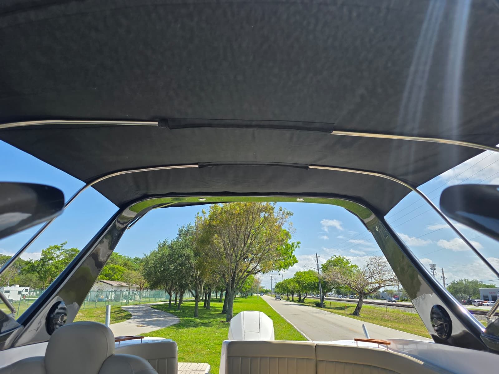 View from inside a boat with a black canopy, surrounded by trees and a road.