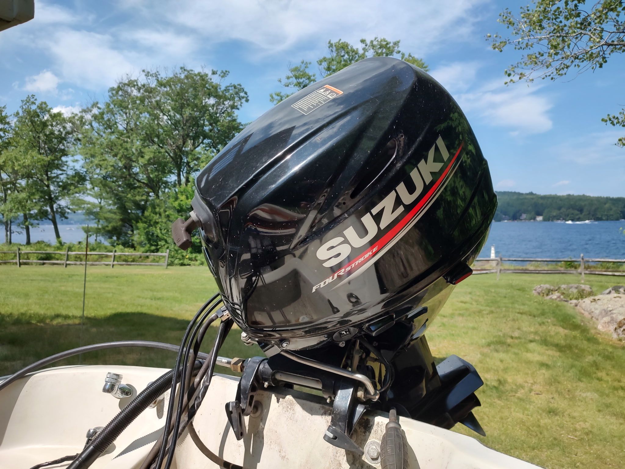 A Suzuki outboard motor on a Boston Whaler Sport 13 boat, overlooking a lake.