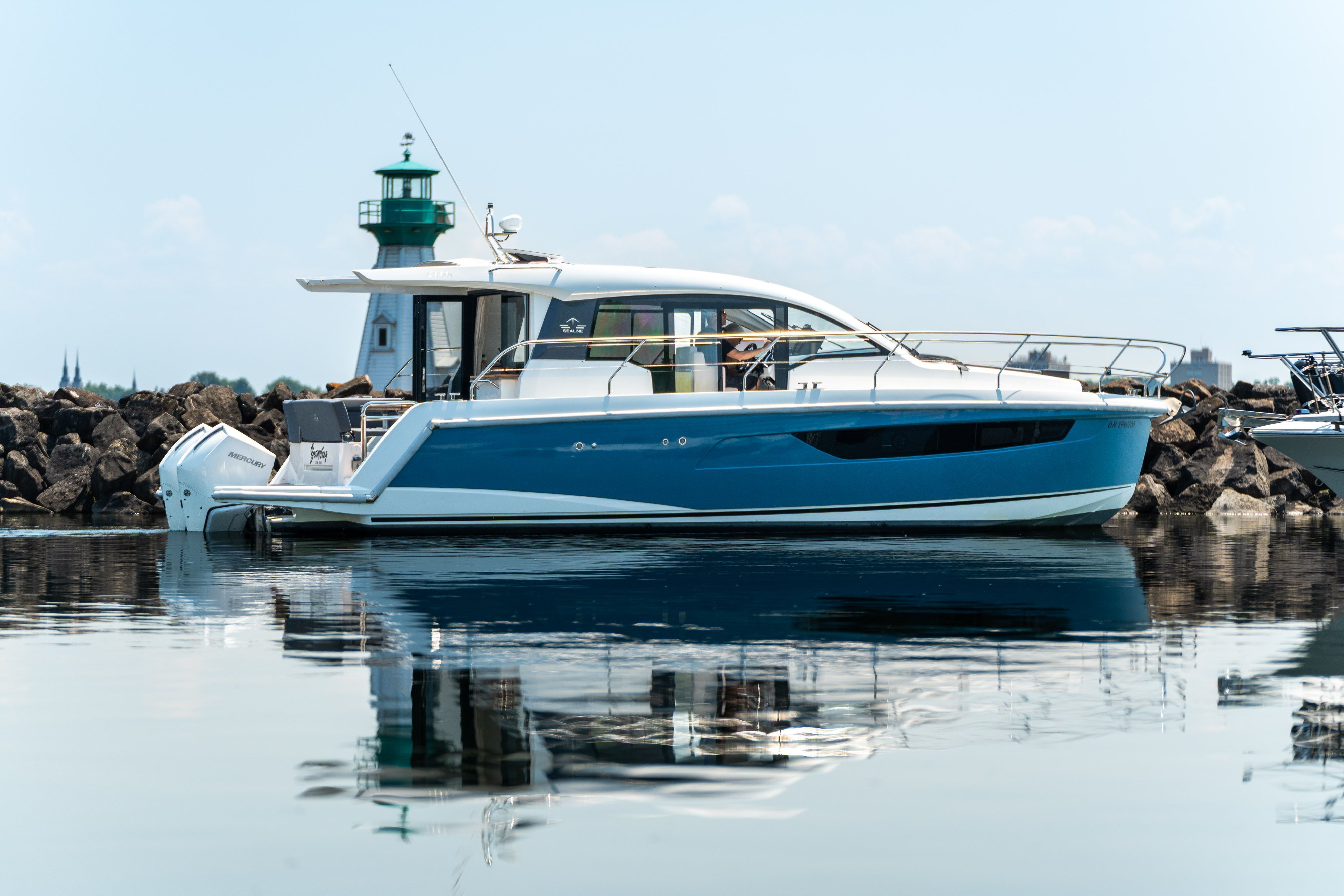 Sealine C335V 2023 near a lighthouse on calm water.