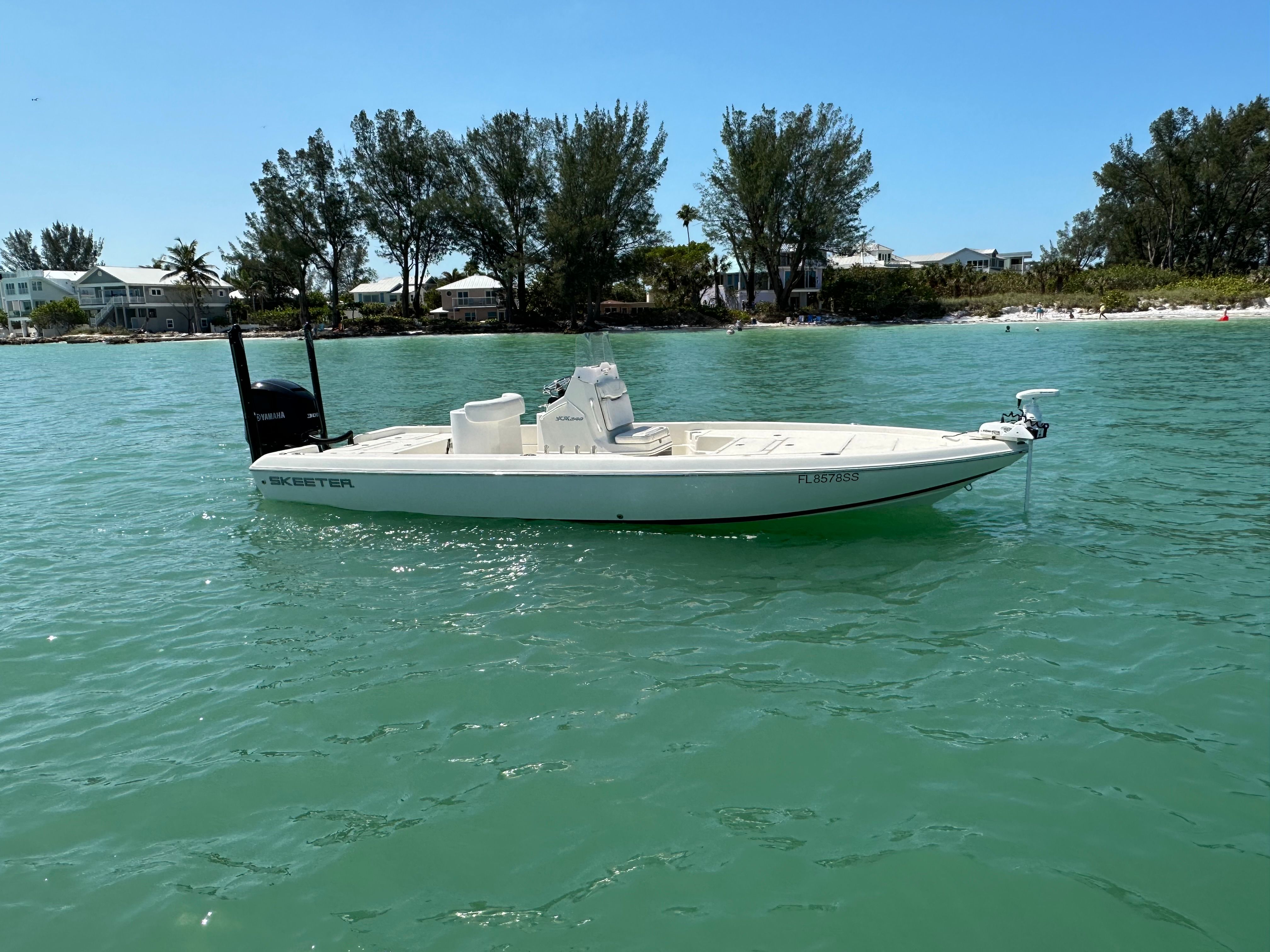 A white boat floating on calm, turquoise water, with trees and houses in the background.
