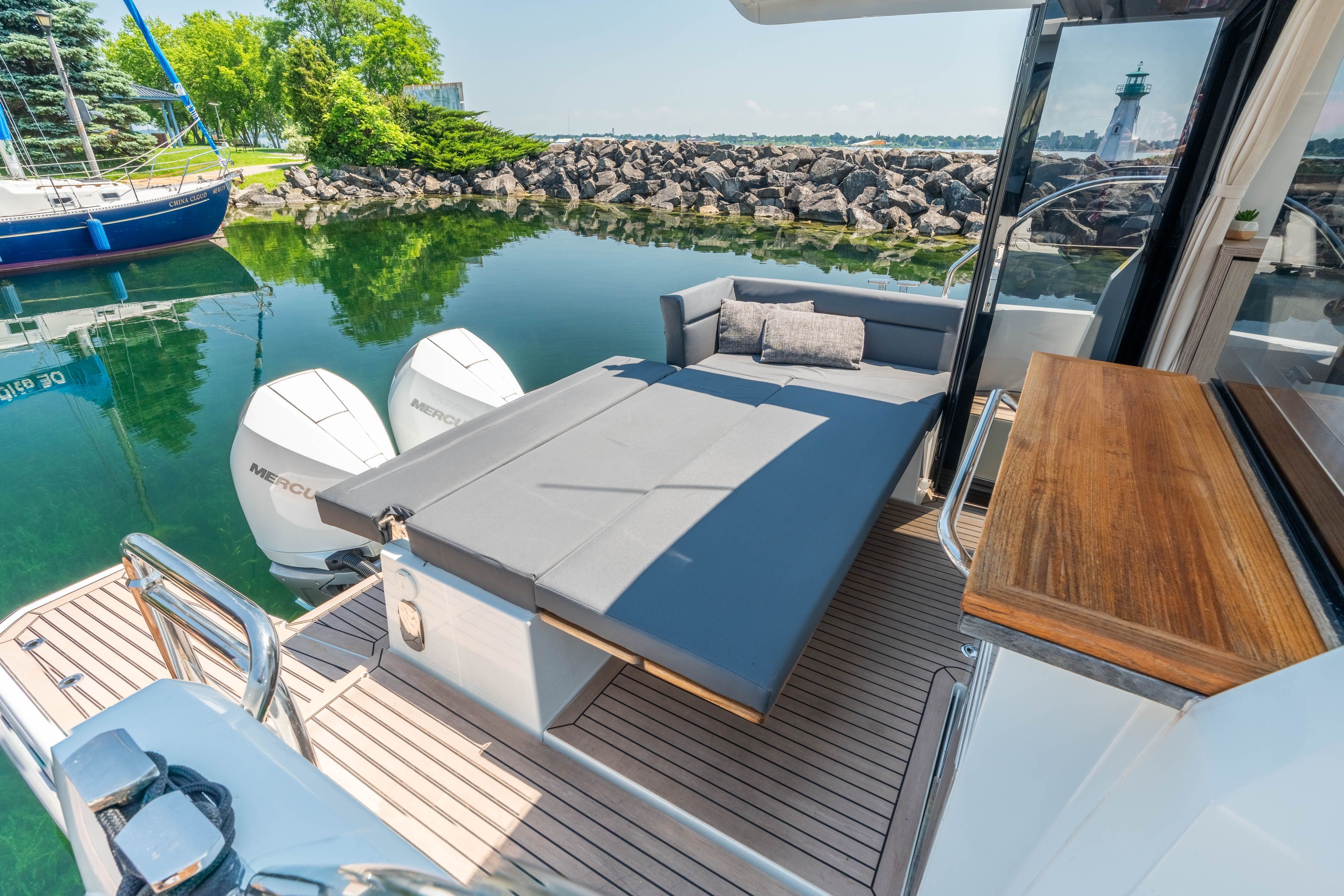 The image shows the stern of a 2023 Sealine C335V with a spacious sun deck and two outboard motors. A lighthouse and calm water are visible in the background.