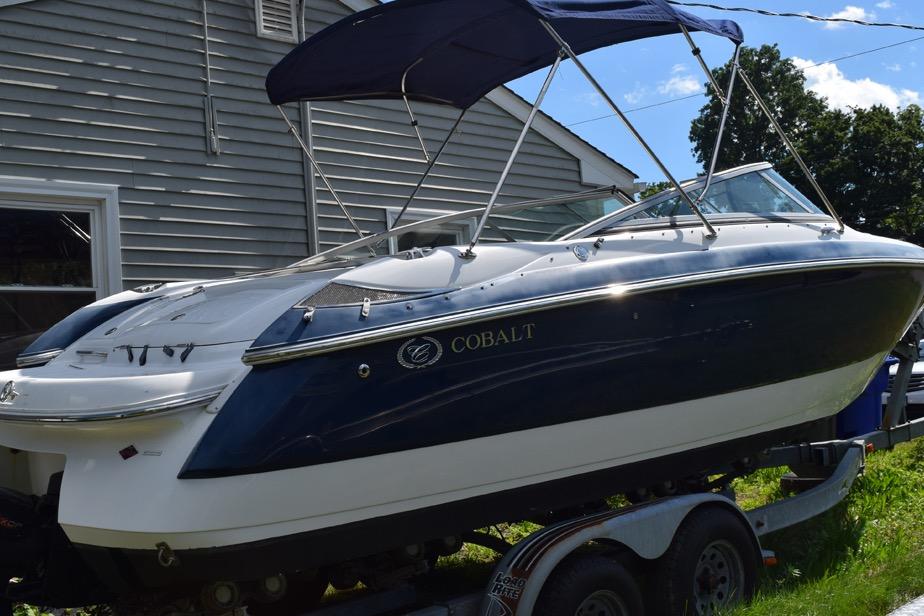 2006 Cobalt 240 boat with blue canopy on trailer, parked beside a house.