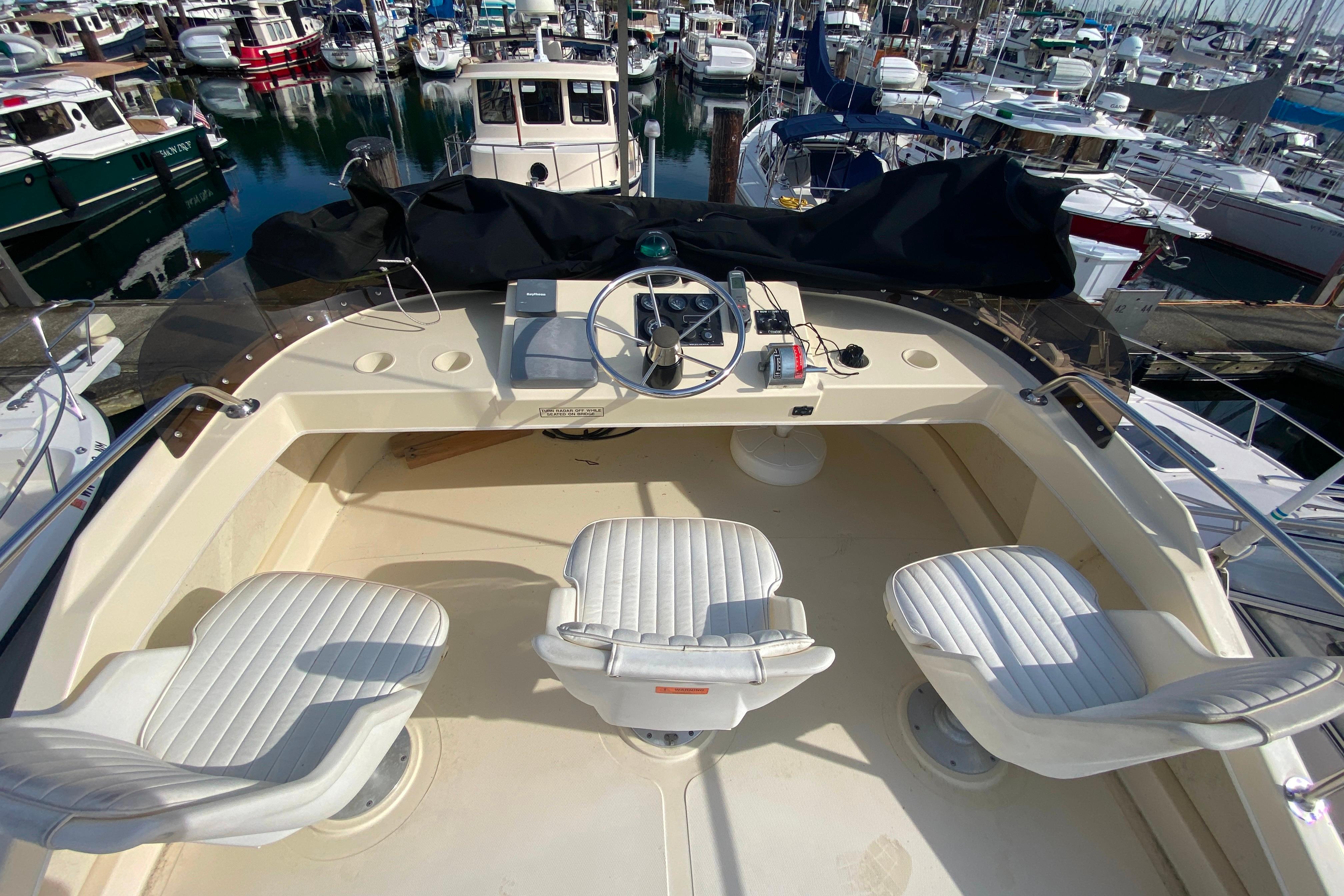 Flybridge of Camano 30 boat with three white seats, overlooking marina.