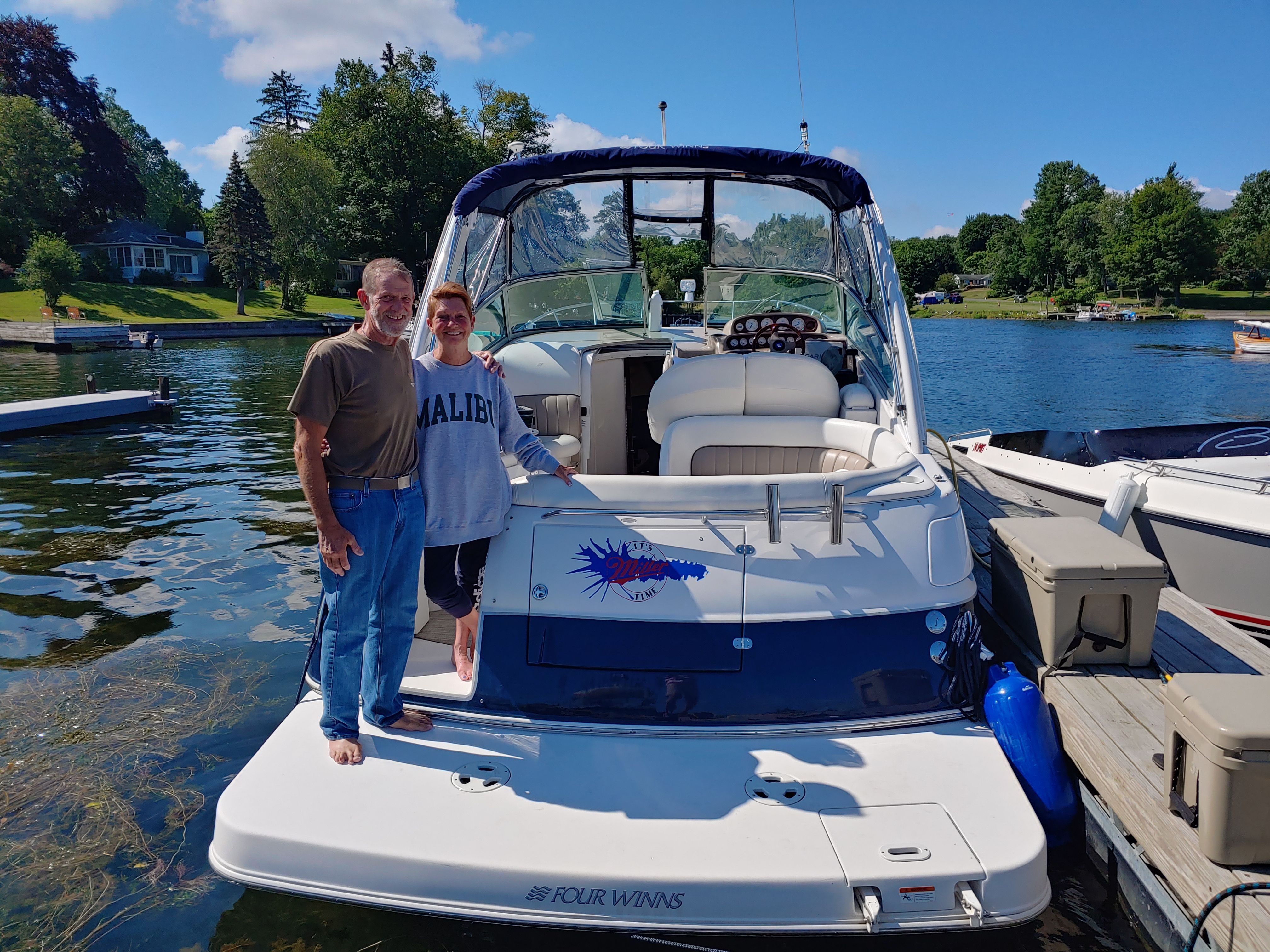 A couple stands on a dock next to a Four Winns 288 Vista boat.